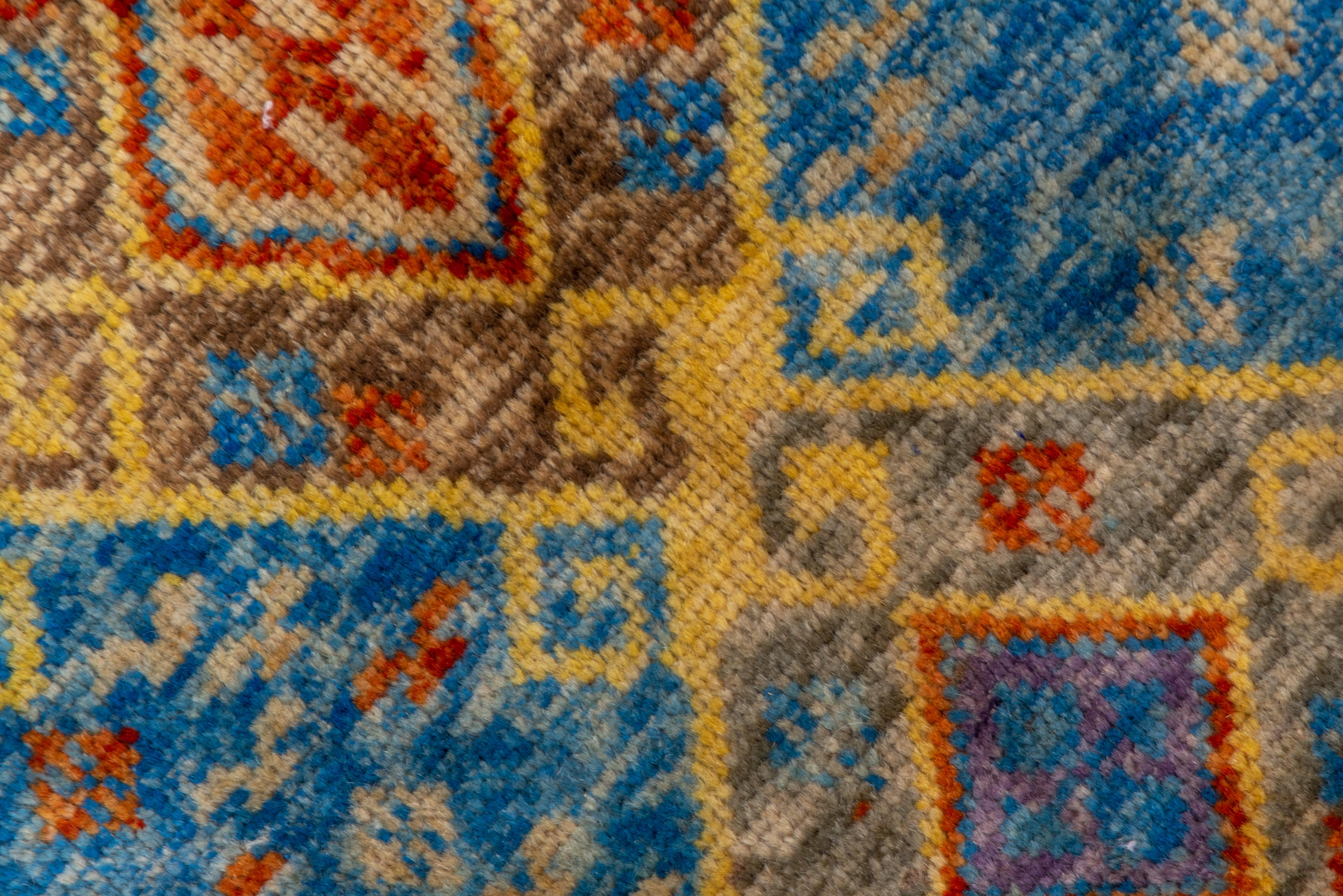 In a geometric Kilim design with only end borders, the watery, broken light blue field displays three columns of joined diamonds detailed in straw, rust and celadon, with small geometric devices scattered around. The colors are broken in a currently