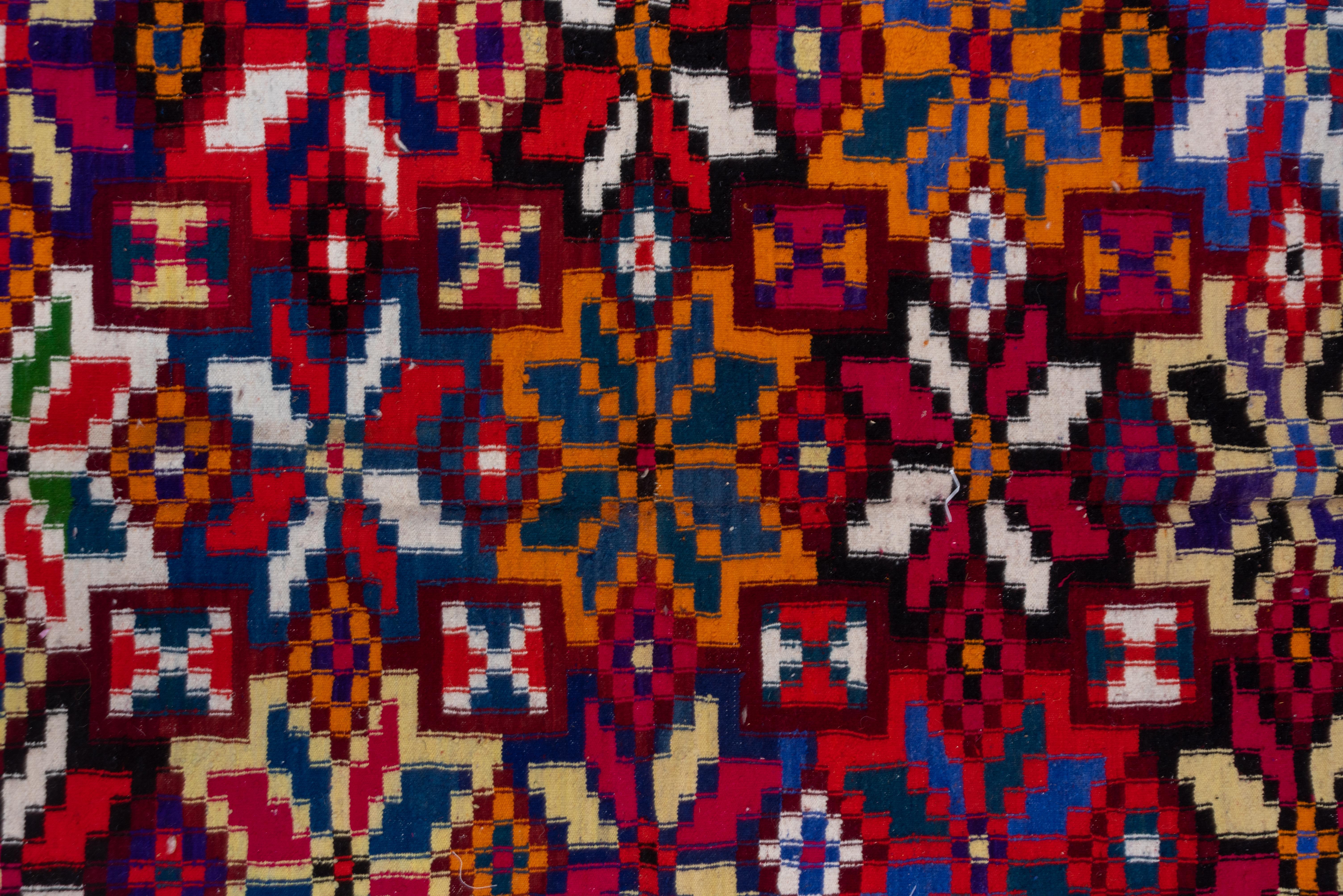A five column pattern of closely set geometric petal-stars is accented in orange, cerulean and straw, all on the black ground of this nomadic tapestry woven carpet. Side borders of in-and-out triangles. As new condition.