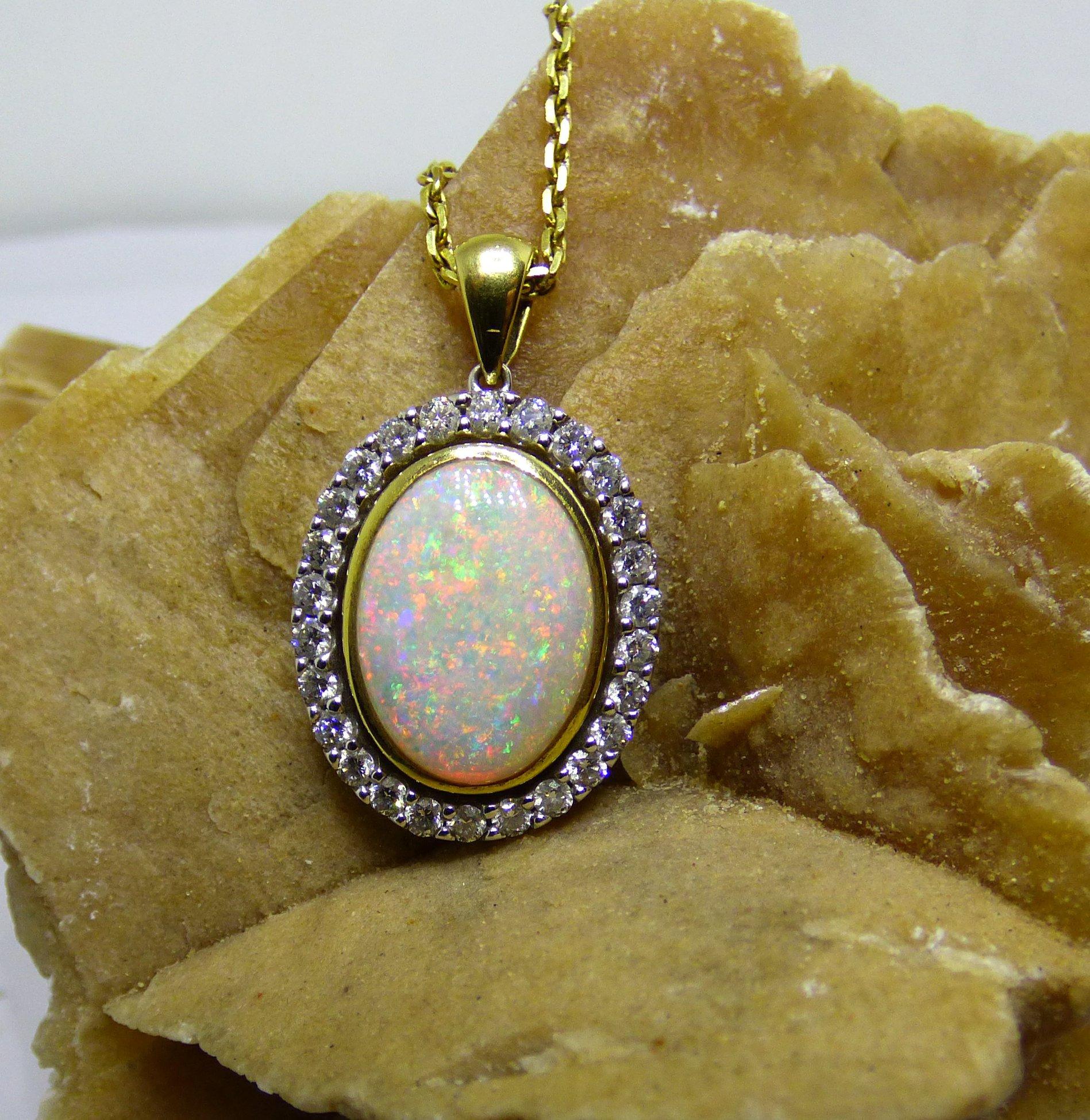 The rainbow of colours that radiate out of an Opal is apparent in this pendant.
This 15X11mm oval Opal (4.5ct.) is surrounded by 26 Diamonds (.98ct.) in a Lapis Jewellers handmade 18K yellow and white gold pendant. The pendant is hallmarked by the