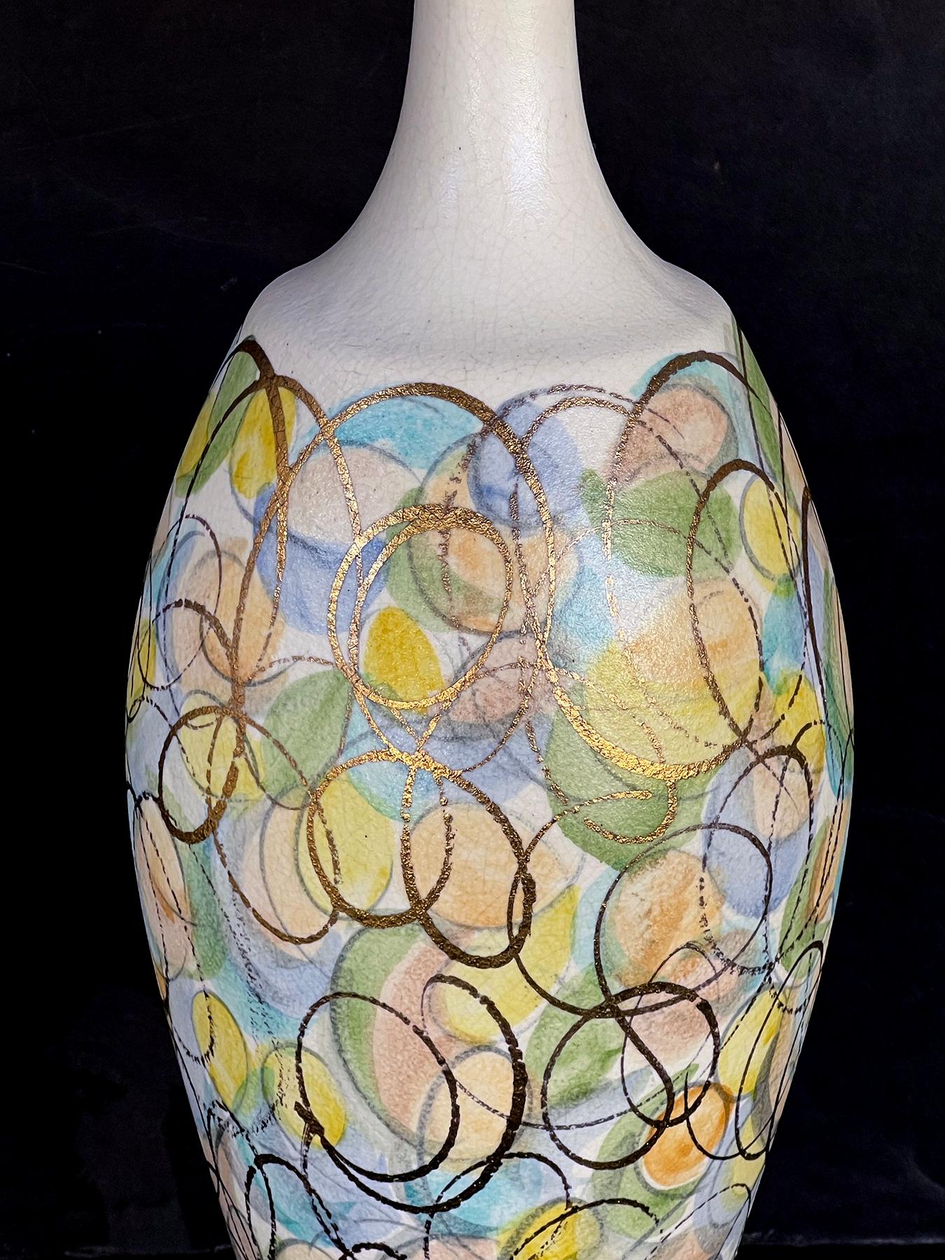 chaque lampe colorée en forme de bouteille est ornée de cercles peints dans des couleurs douces de bleu, vert, pêche et jaune avec un tourbillon d'or, le tout sur un fond émaillé ivoire ; supportée par des bases en métal peintes en brun ; hauteur :