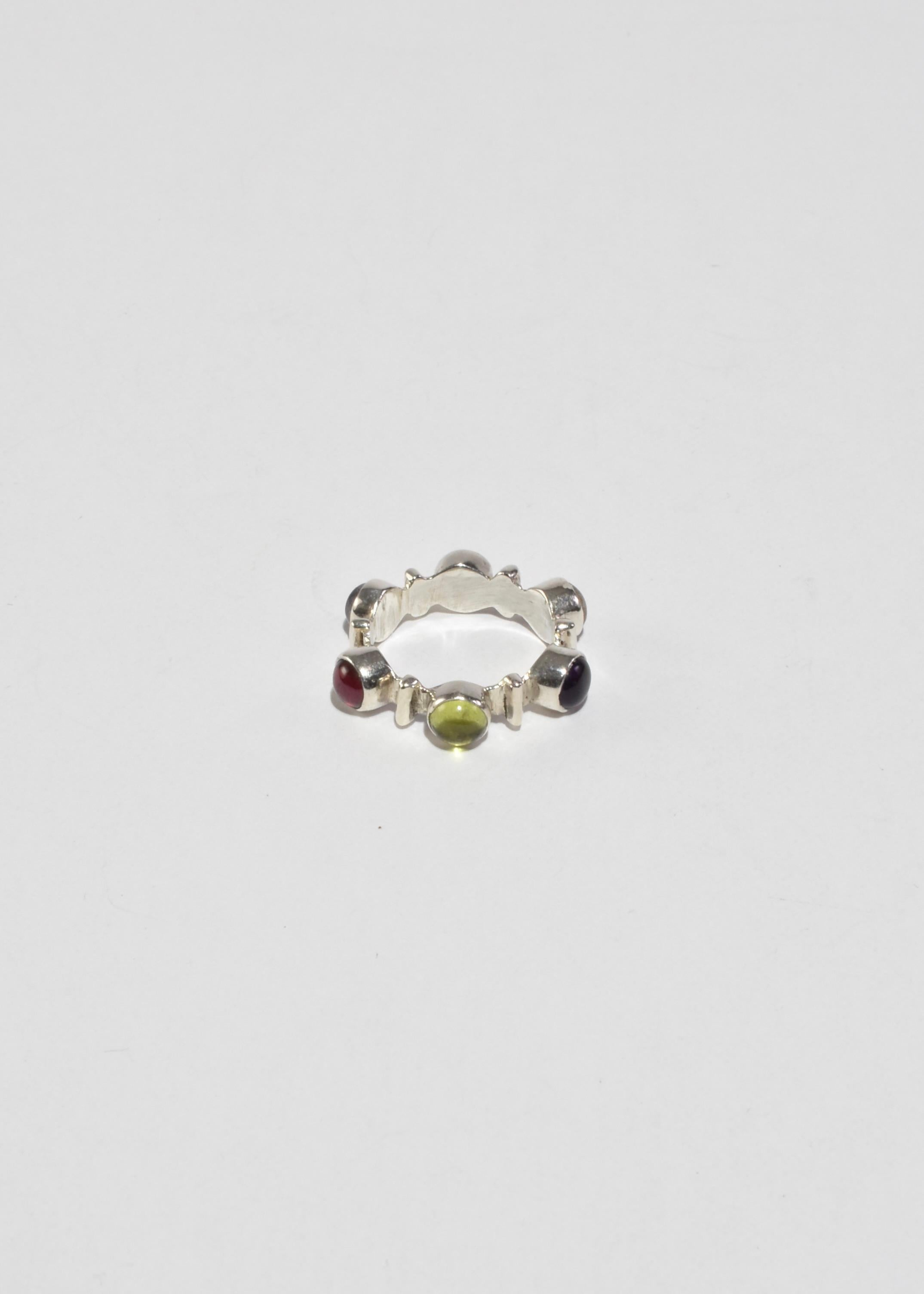 Vintage silver band ring with round colorful multi stone cabochons. Stamped 925.

Material: Sterling silver, amethyst, peridot, quartz, garnet, iolite, ruby.