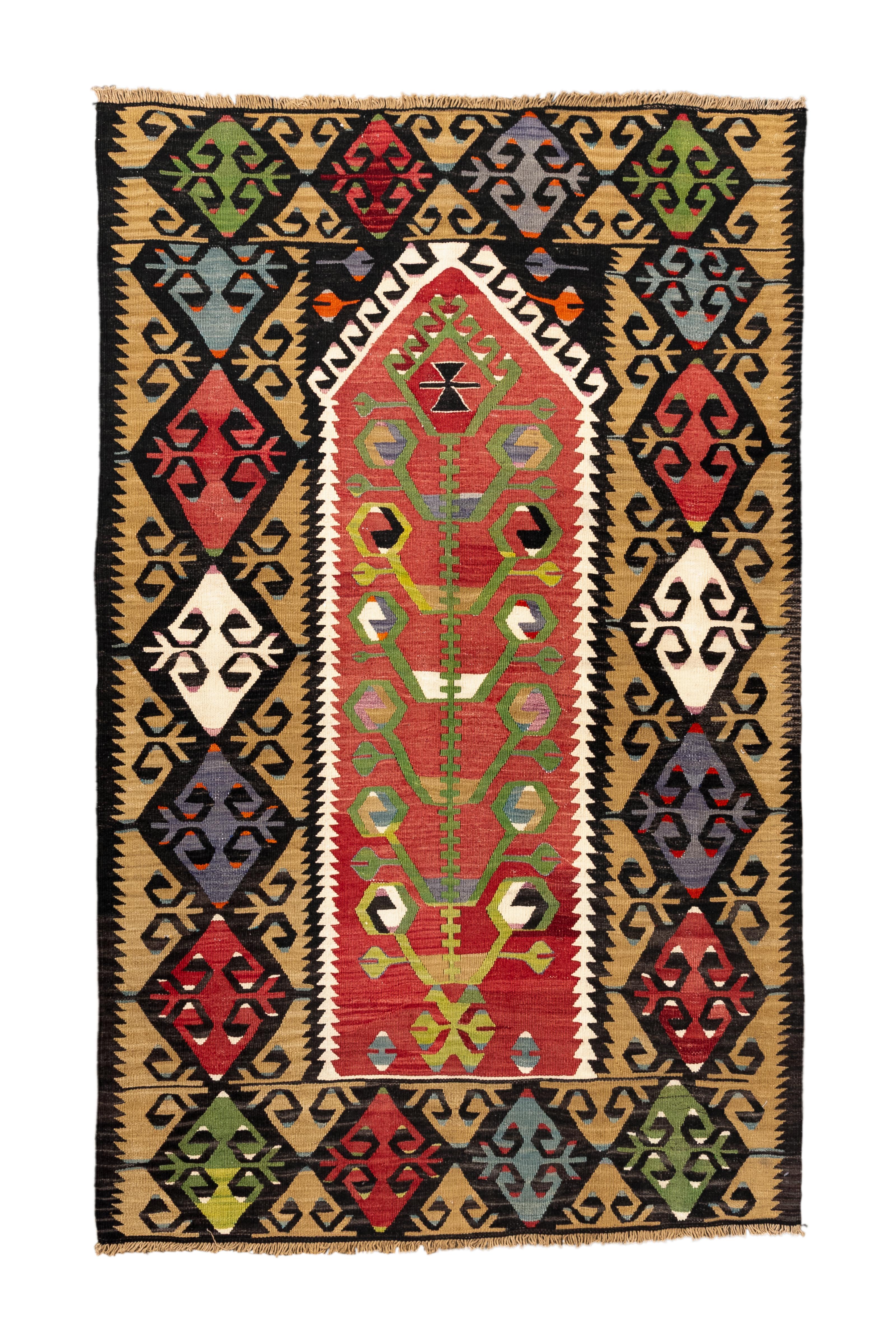 Questo kilim turco vintage è una vivida celebrazione del simbolismo tribale e del colore, incentrata sul motivo stilizzato dell'Albero della Vita. Il pannello centrale, in grassetto rosso, ospita un albero verde simile a una vite affiancato da bordi