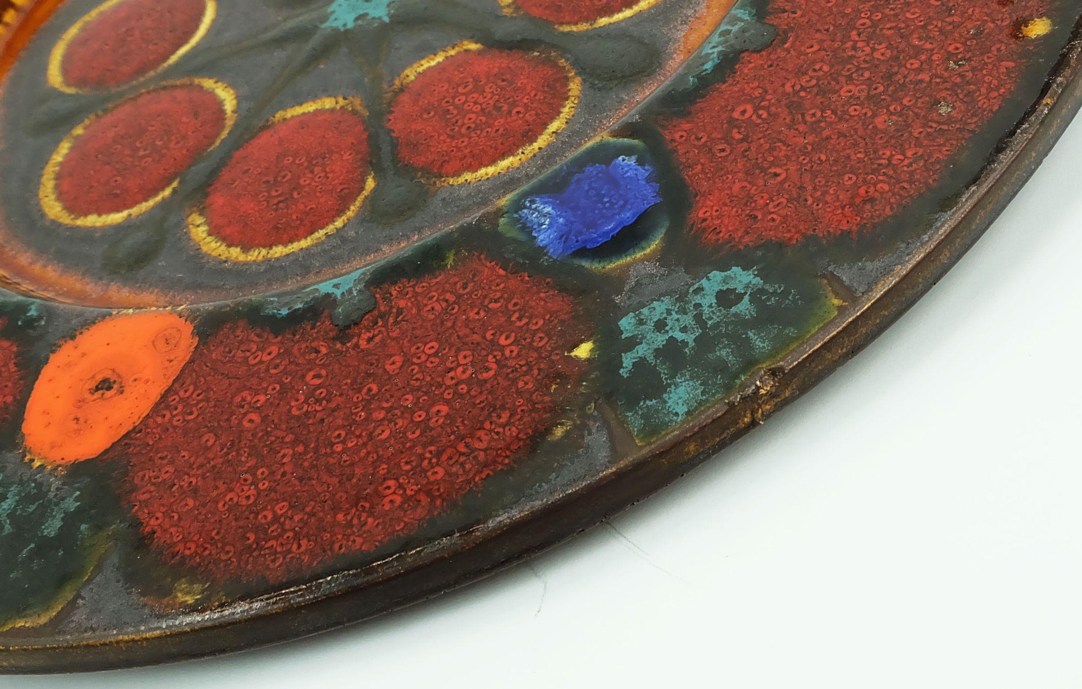 Outstanding large mid century ceramic plate in bright colors combined with a shimmering copper glaze and black fat lava glaze. Manufactured by Grünstadt Keramik, 1960s to 1970s. Includes a wall hanger. 

Dimensions in cm:
Diameter 43.5
