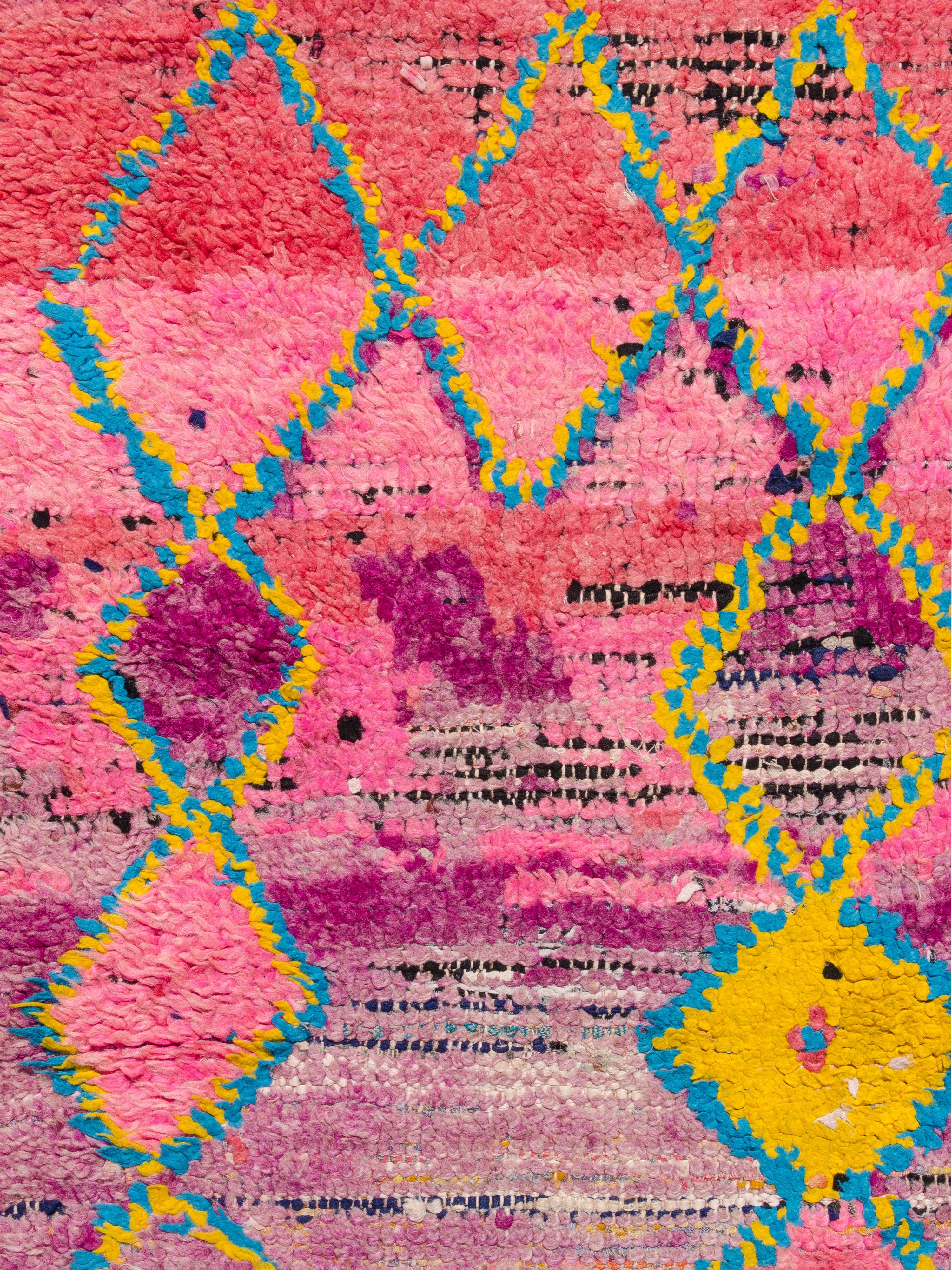 Une coulisse de Boujad présentant une composition spontanée de chaînes de losanges ouvertes et remplies, entrecoupées de formes en zig-zag. Tissé dans une palette très saturée de violet vif, magenta, rose corail, rouge feu, jaune et bleu ciel. Une