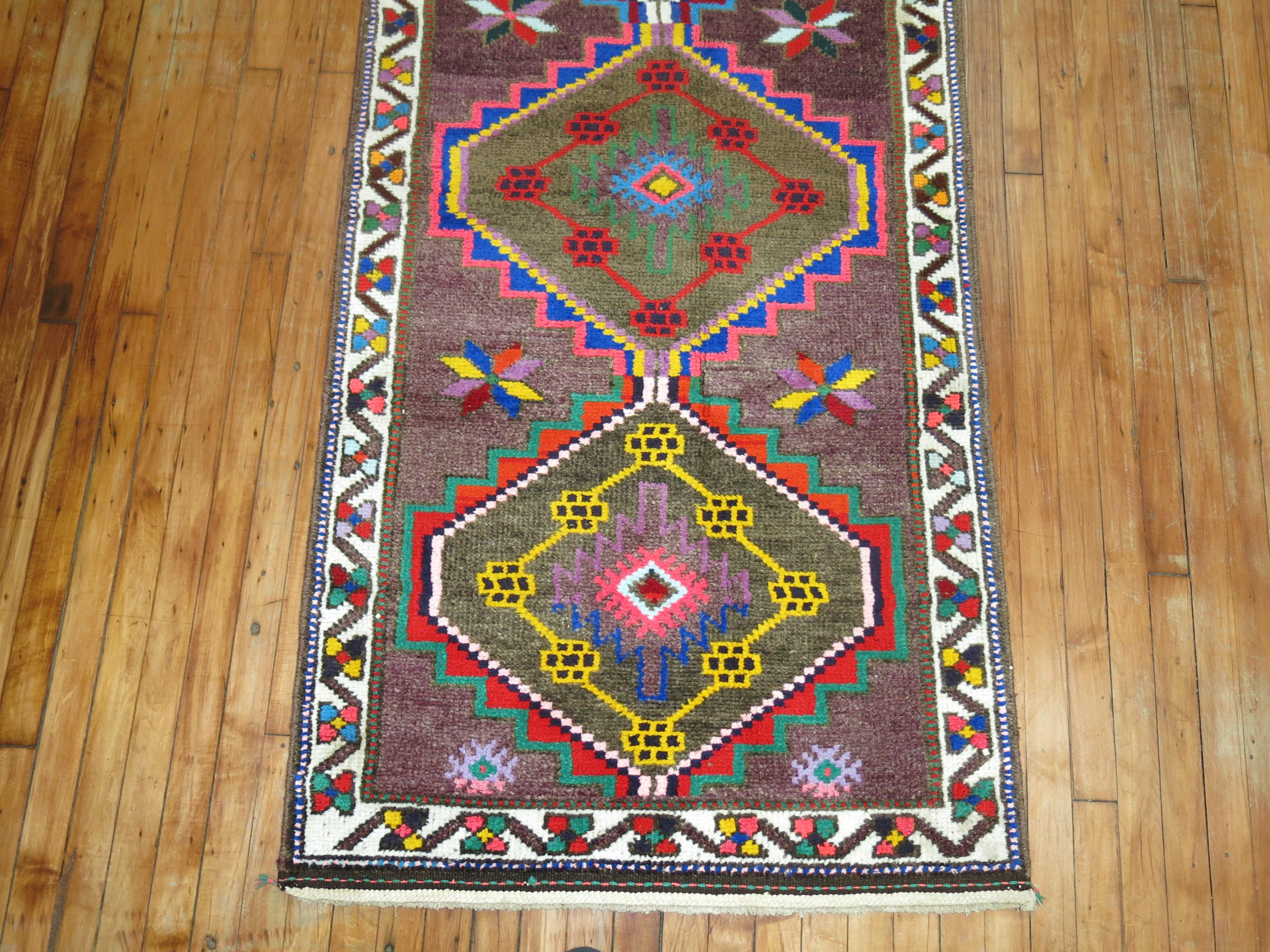 A fun Turkish Anatolian runner with a flashy array of electric colors on a purple color ground, circa mid-20th century. 
Measures: 3' x 13'10''.