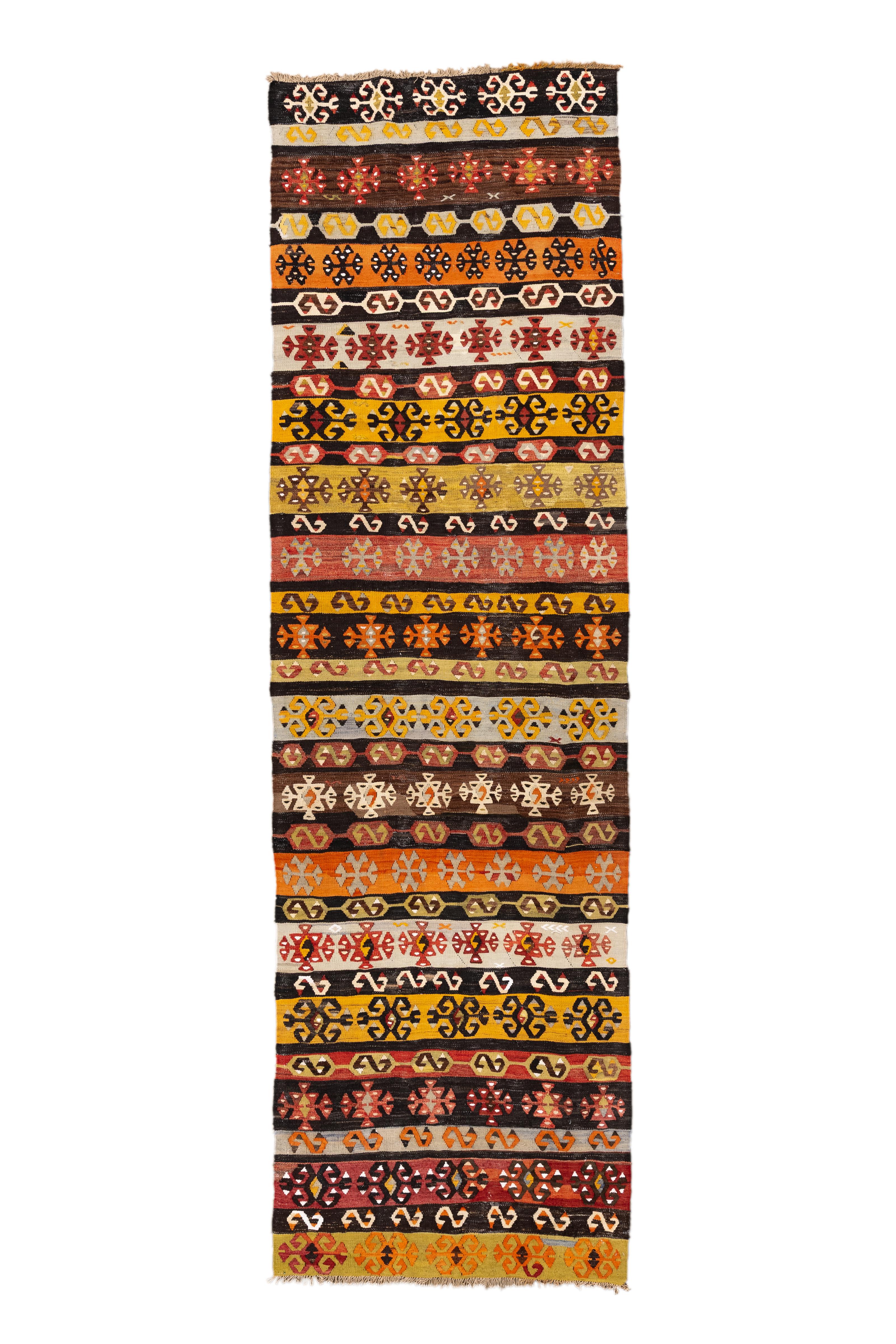 Dieser türkische Kelim-Läufer im Vintage-Stil zeigt eine üppige und rhythmische Komposition aus bunten Stammesstreifen. Abwechselnde Streifen in Safran, Ziegelrot, Ocker, Schwarz, Elfenbein und Rost sind mit symbolischen anatolischen Motiven