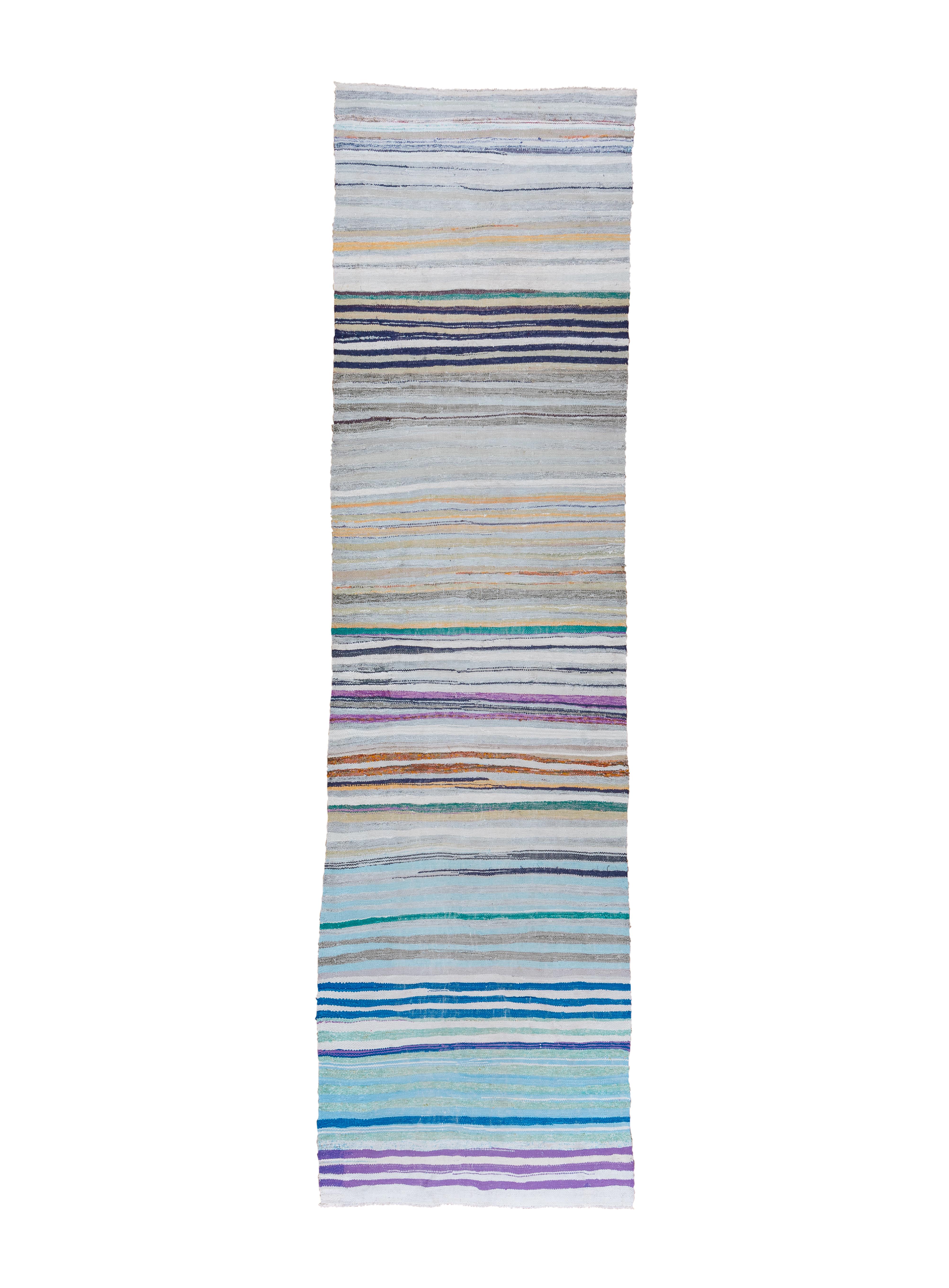 This pileless runner is composed of fabric strips from garments or household décor, bound by thin cotton cords. The colours vary throughout, in no particular order, including shades of blue, creams, teal, brown, beige and rust. Ideally the strips