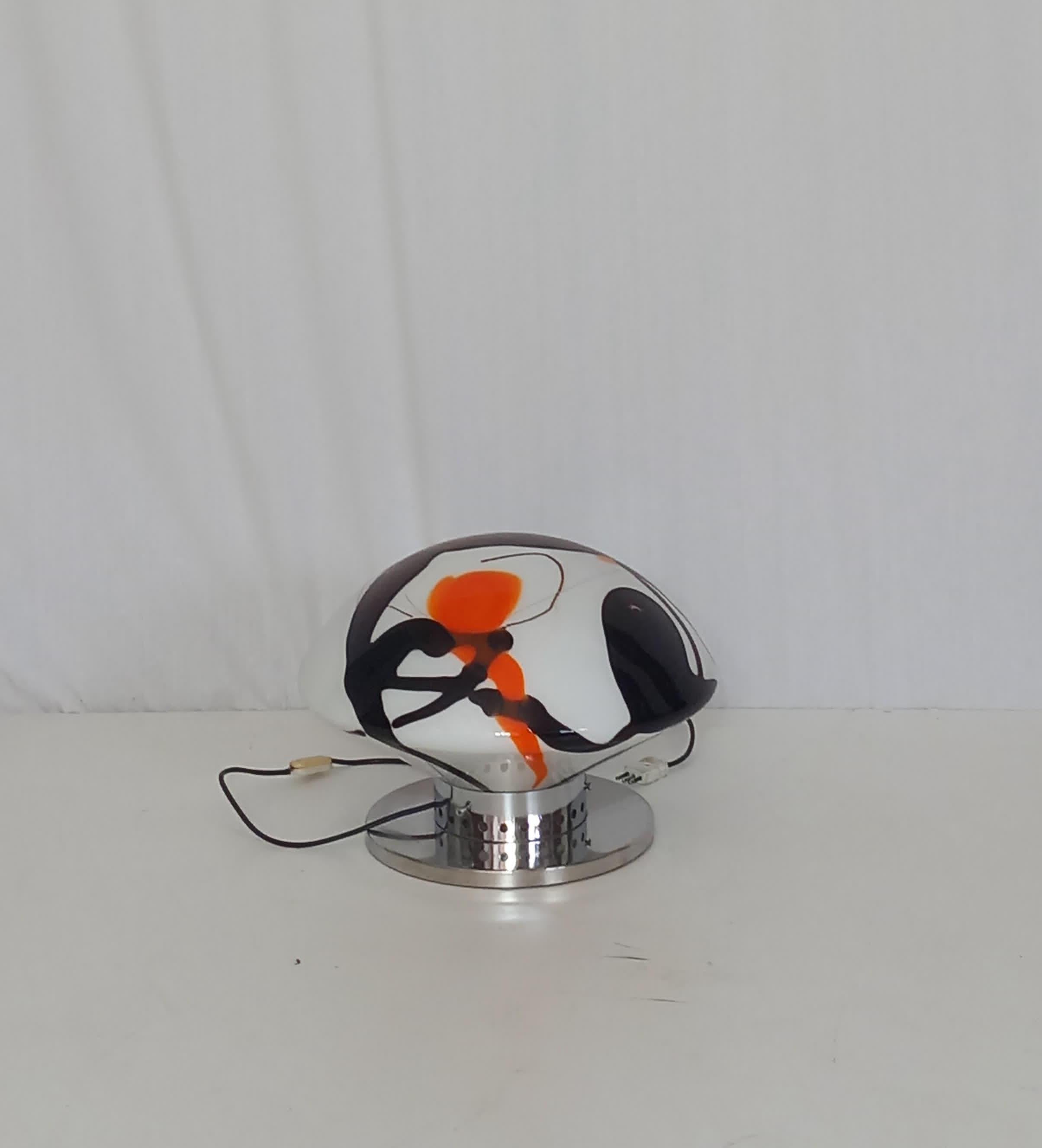 Add a touch of mid-century charm to your space with this peculiar round-shaped table lamp, designed and produced in the 1950s. A true statement piece, it features a striking combination of opal glass and metal elements, highlighting the timeless
