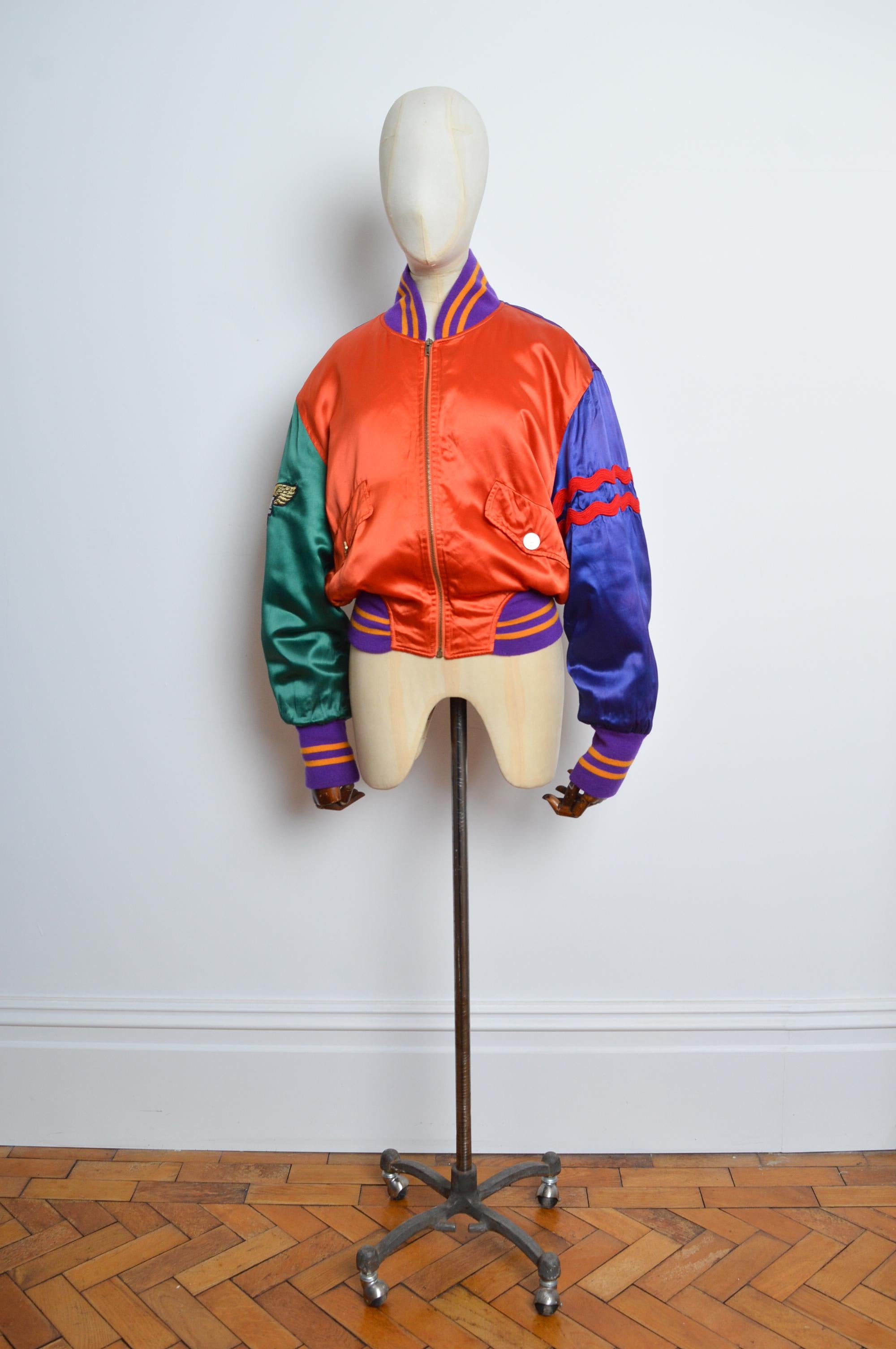 Bomber colorato 'LOVE IS IN THE AIR' anni '90 di Moschino in raso con dettagli applicati, toppe e ricami!
MADE IN ITALY.
Caratteristiche: maniche lunghe, silhouette Varsity, tasche in vita e zip sul davanti Chiusura. 
Taglia - Si adatta meglio al