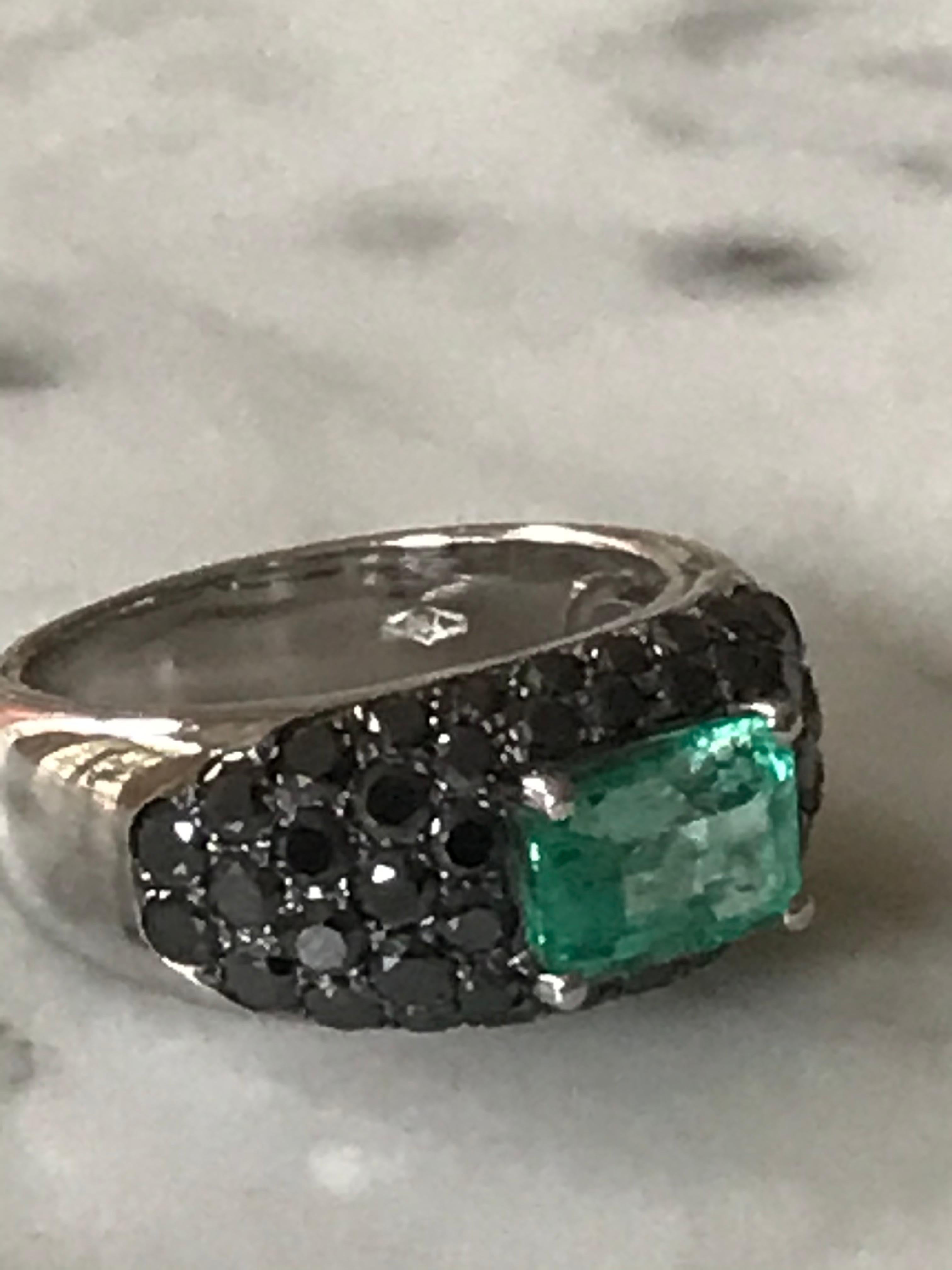 Emerald cut 2 carat Columbian Emerald ring mounted in 18k white gold
set with black diamonds. A sought after emerald from the Muzo mine in Columbia, beautifully offset by a host of brilliant cut black diamonds creating a dramatic backdrop for the