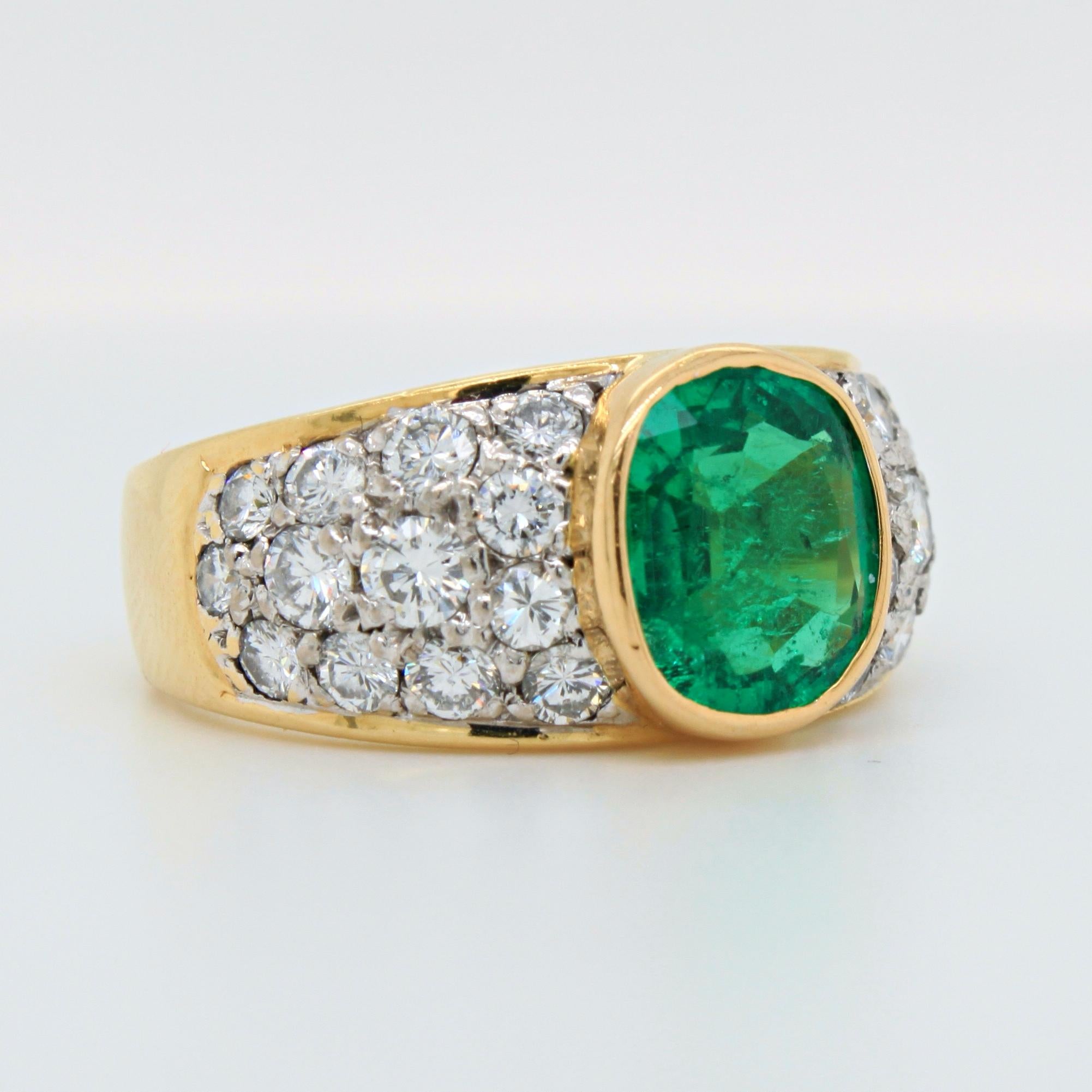 A Colombian emerald and diamond ring in 18k yellow gold. The flat emerald cushion has a strong crystal and beautiful deep green colour, with a lovely jardin adding to the allure of the gemstone. It weighs approximately 1.66 carats and is of