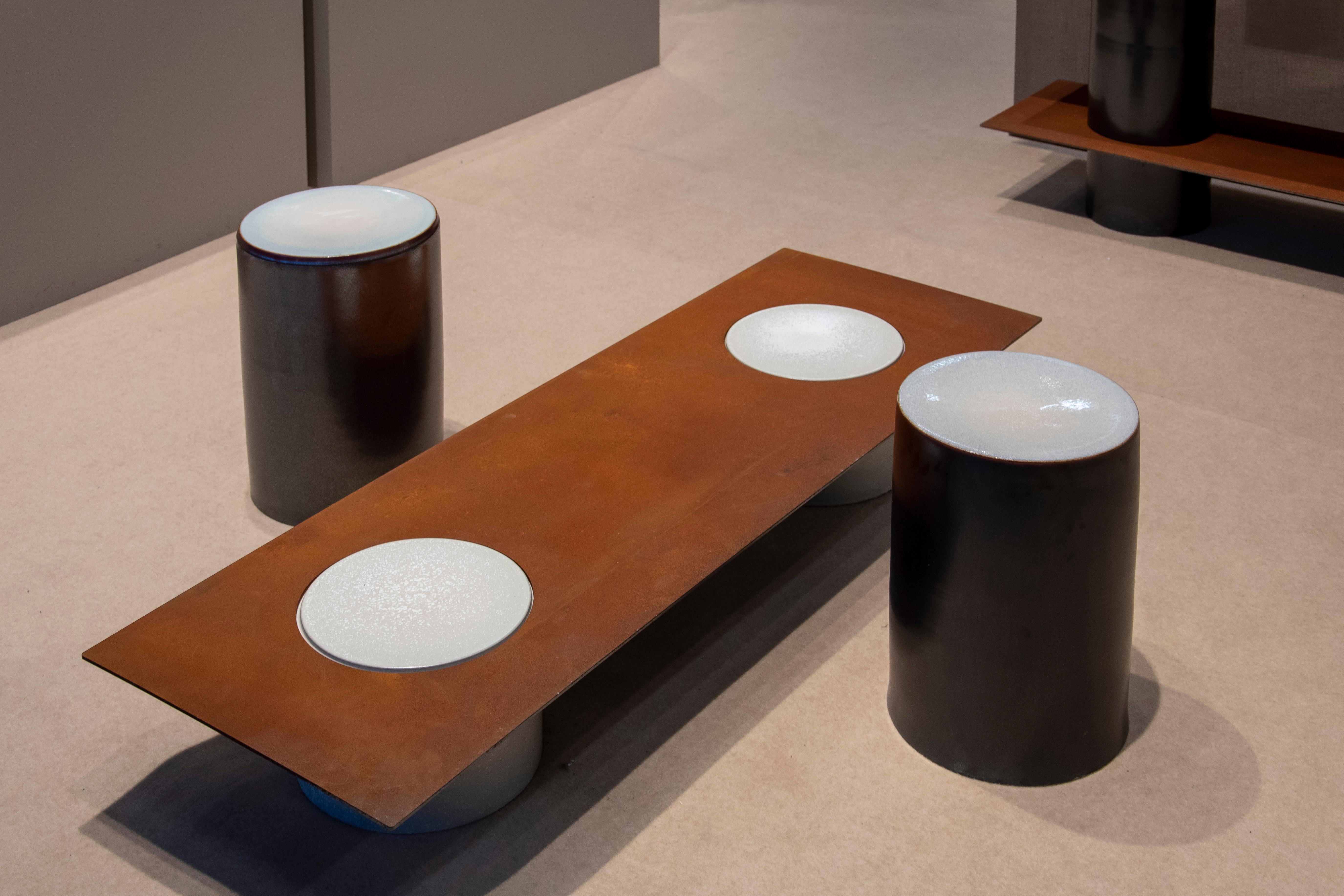 Porcelain cylinders and corten steel plates form the basic elements of this series, with which it is possible to create shelving, side tables, low tables and stools. The porcelain parts are hand thrown, trimmed, glazed and fired at 1300 C by the