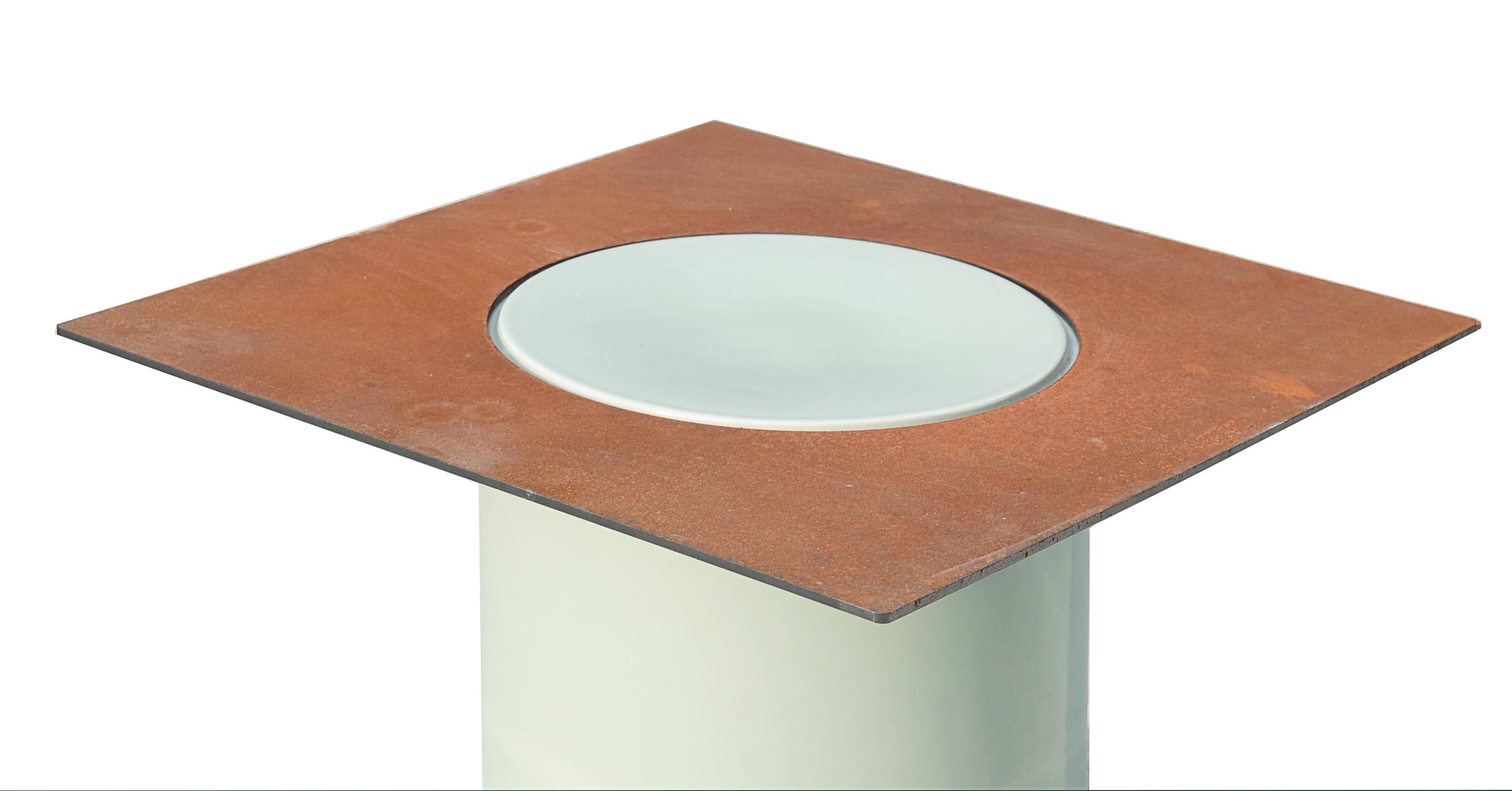 Les cylindres en porcelaine et les plaques en acier corten constituent les éléments de base de cette série, avec lesquels il est possible de créer des étagères, des tables d'appoint, des tables basses et des tabourets. Les pièces en porcelaine sont