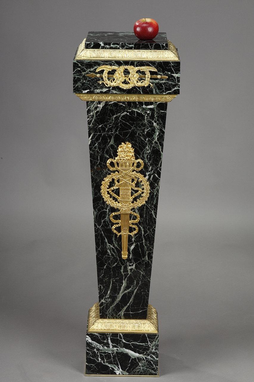 Sumptuous column sheath in Vert de Mer marble of square section. The front face is decorated with a flaming torch, entwined with ribbons and a crown of branches of thorns in gilded and chased bronze. The gilded bronze mounts are decorated with a