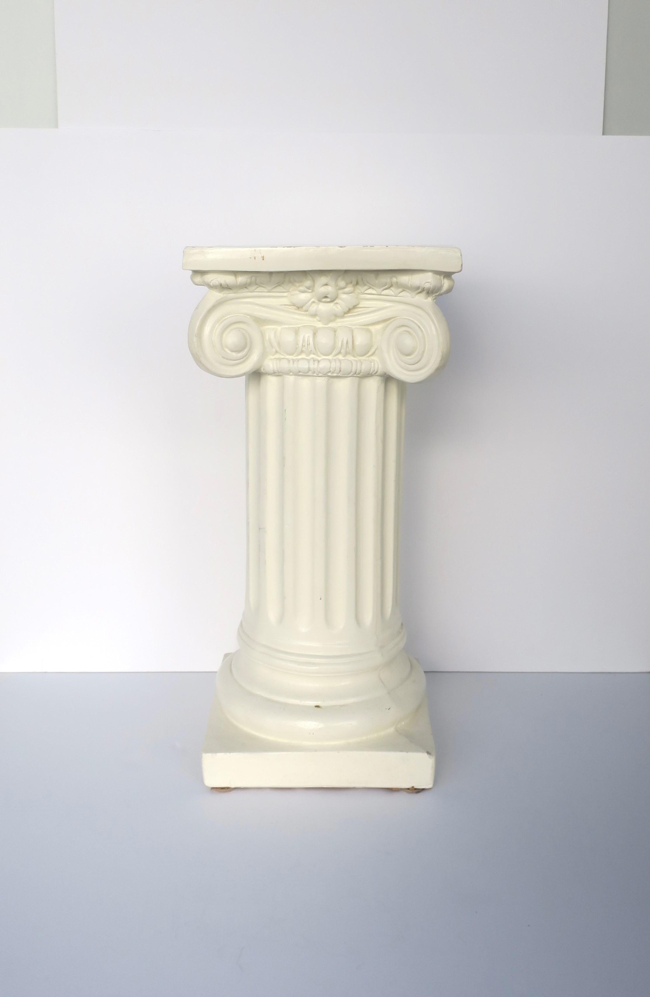 A glazed plaster Grecian Ionic order column pedestal stand in the Neoclassical style, circa mid to late-20th century. Piece is an off-white glazed plaster. A great piece for a sculpture, plant, books, light/lamp (shown with books and globe light),