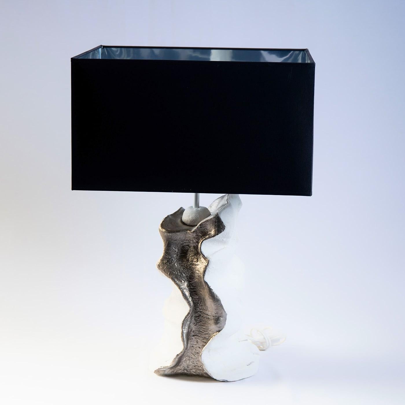The existential question of how humanity could defy eternity inspired artist Angelo Salemi to craft this singular table lamp. A luxurious and elegant lampshade bleak con the outside and silvery on the inside stands above a sinuous ceramic base with