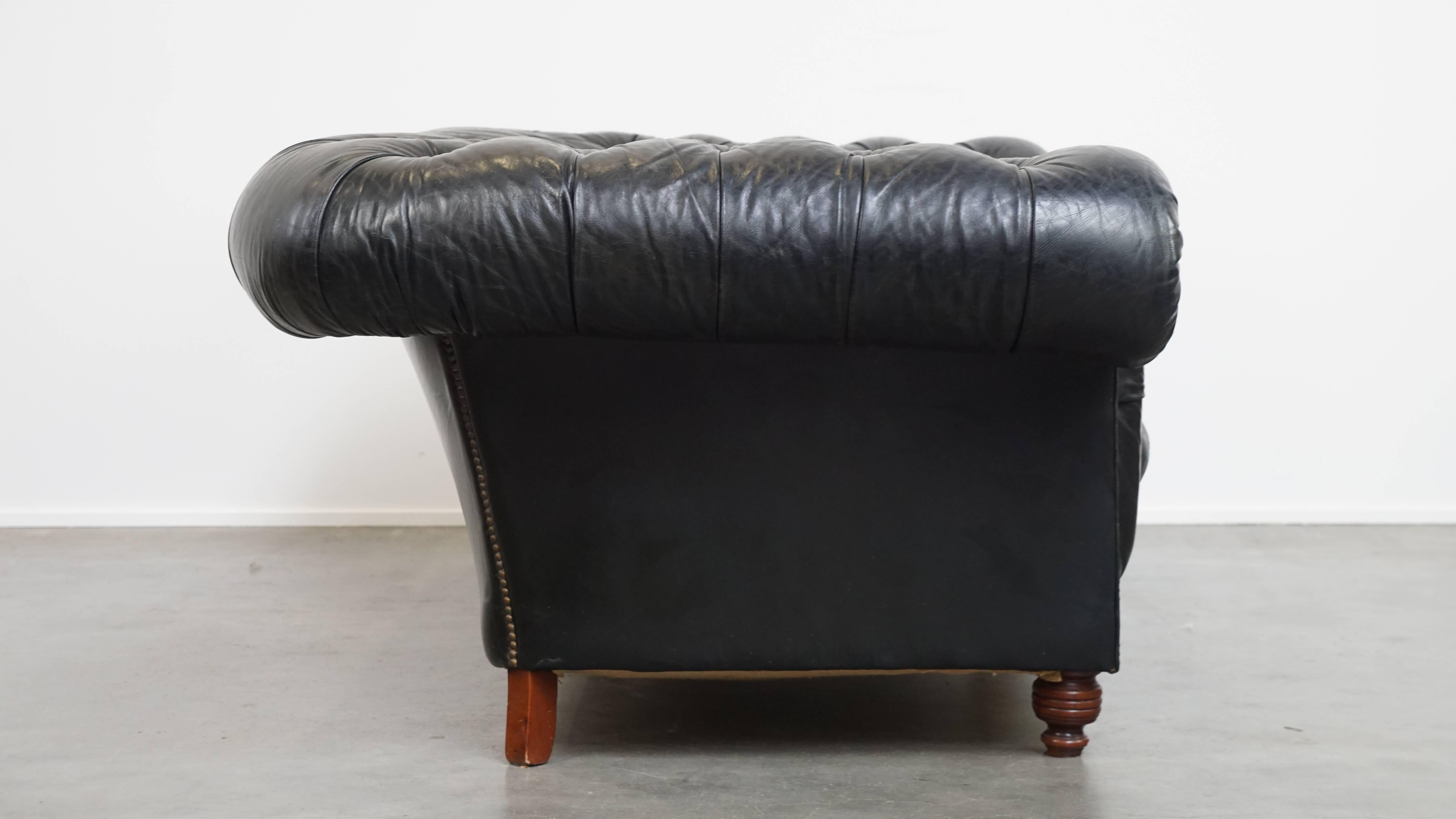 Dieses elegant geformte schwarze Chesterfield-Sofa aus Leder fügt sich mühelos in nahezu jeden Einrichtungs- und Dekorationsstil ein. Mit seinem tiefen Sitz und den daunengefüllten Kissen bietet er ein sehr bequemes Sitzerlebnis.

Mit seinen breiten