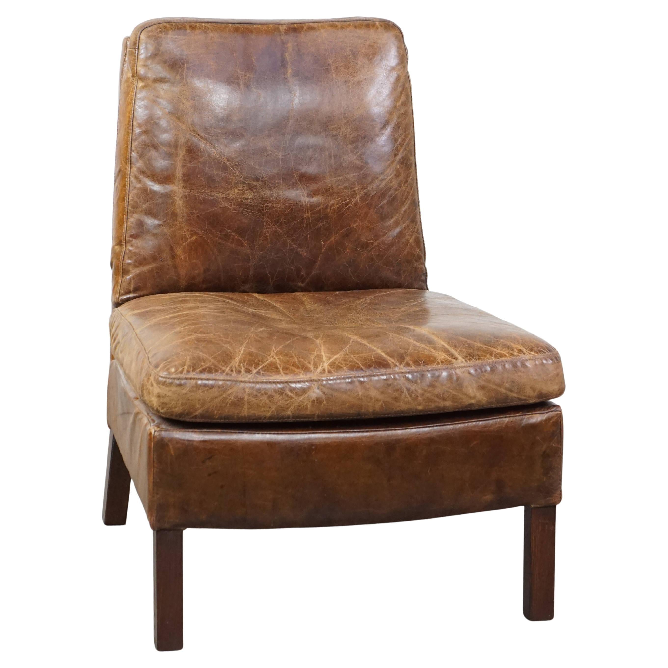 Comfortable cow leather lounge chair with a unique design and beautiful patina For Sale