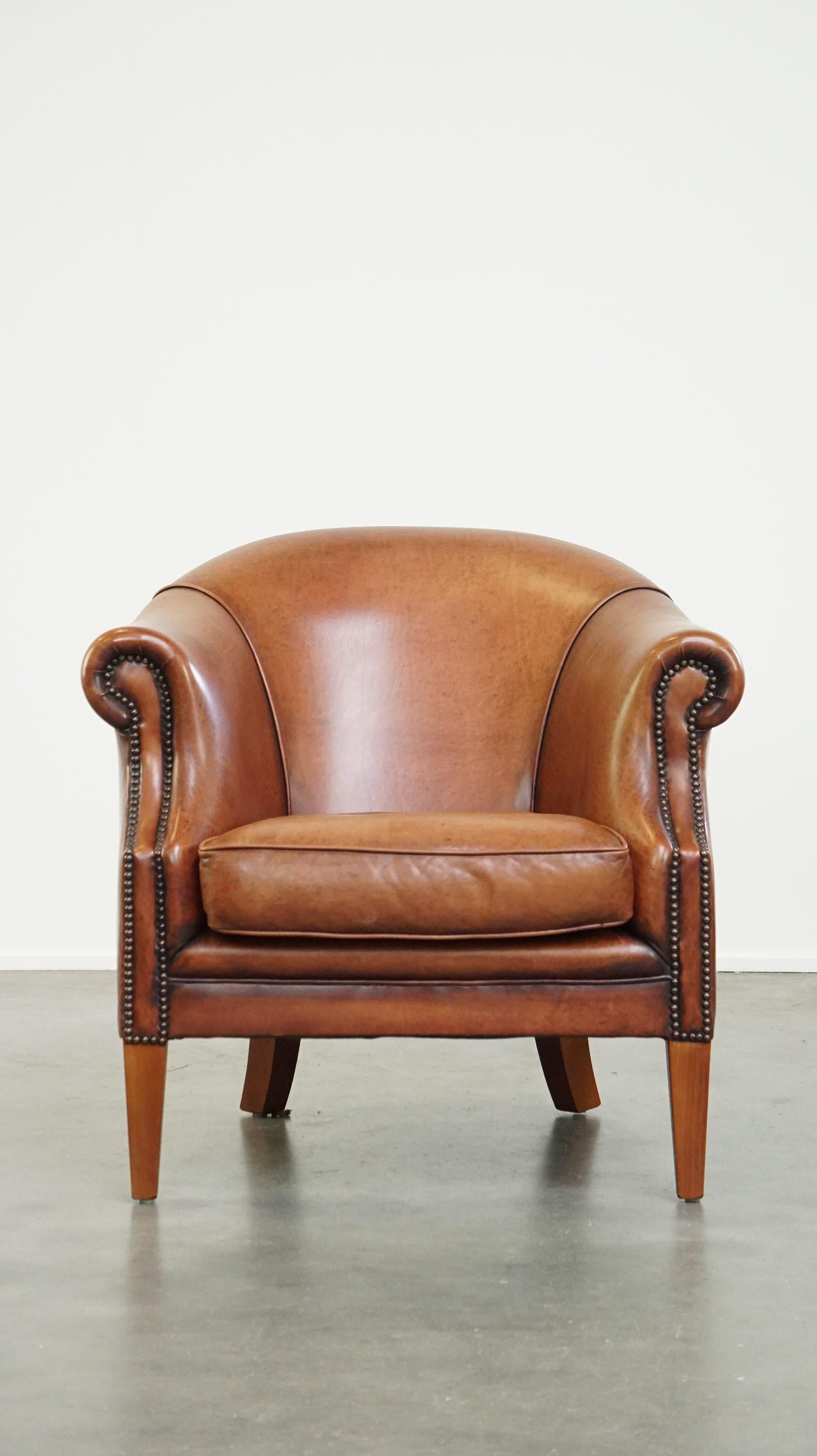 This fantastic leather club armchair has developed a wonderful patina from years of use. It features a loose seat cushion and offers excellent seating comfort. Neatly finished with decorative nailheads, its warm color makes it easy to integrate into