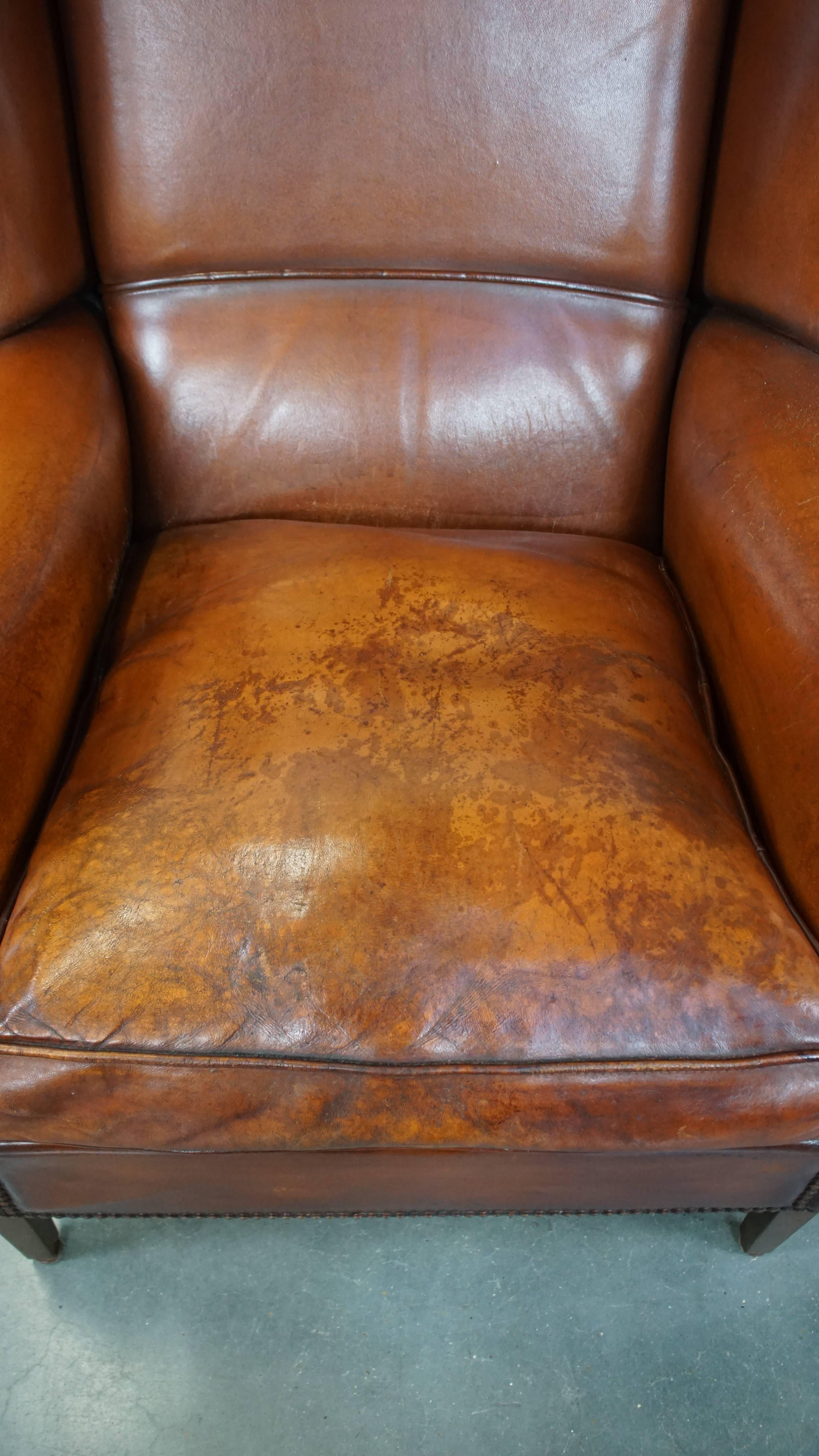 Leather Comfortable sheepskin leather wingback chair with a warm color scheme and patina For Sale