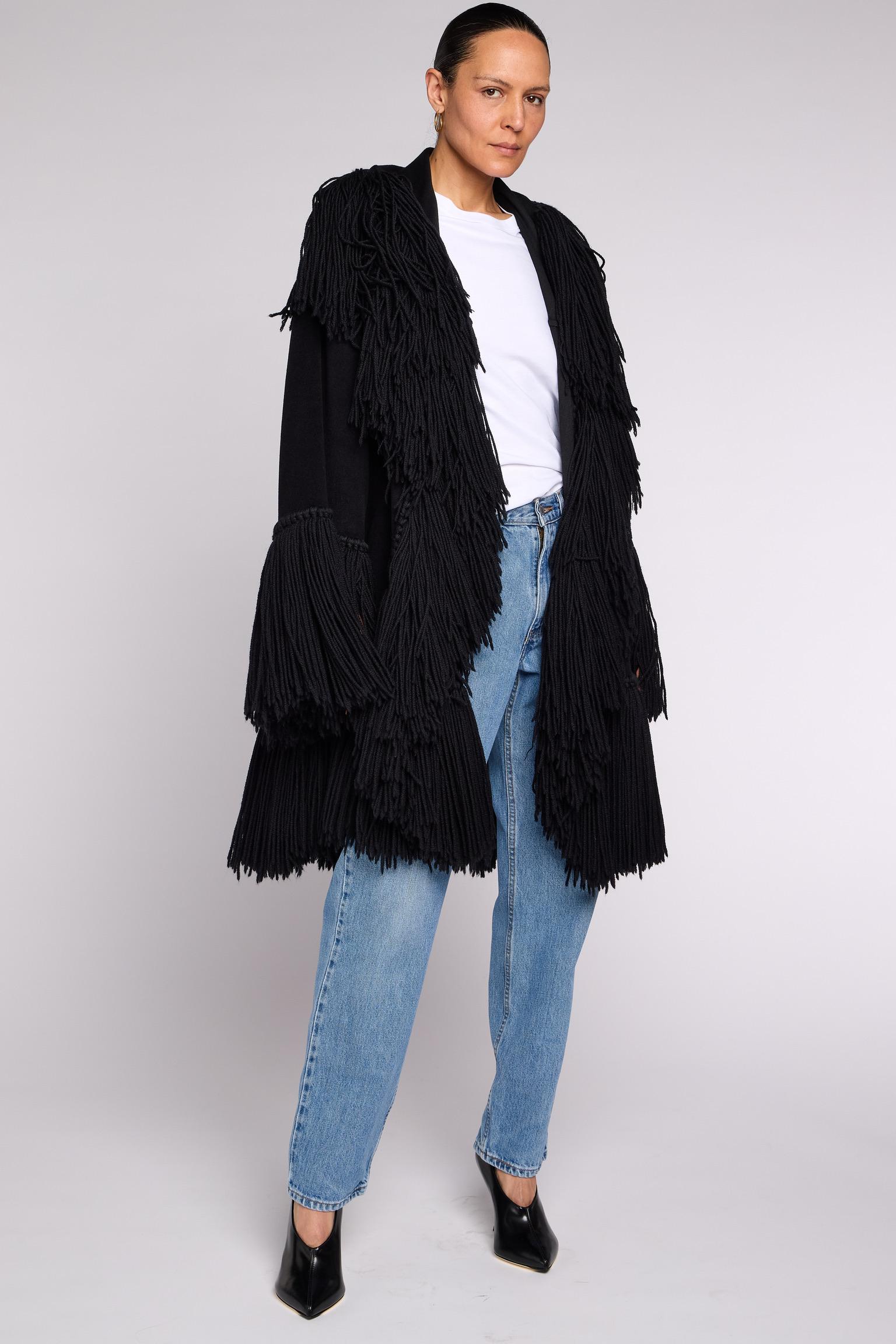 1980 Comme des Garçons par Rei Kawakubo
Manteau oversize en laine noire avec franges exagérées.
