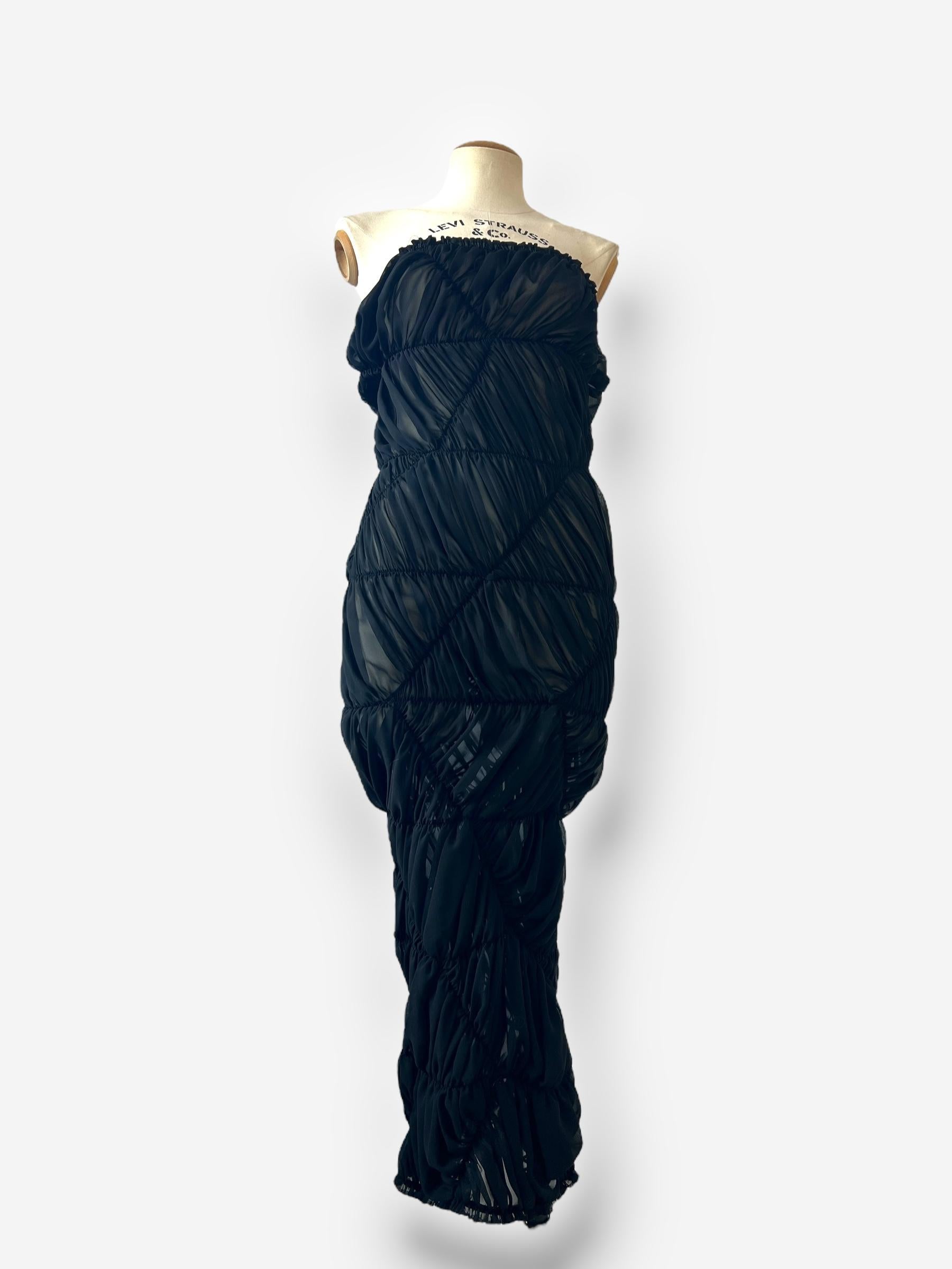 Eine auffällige und skulpturale Comme des Garçons-Kreation aus dem Jahr 2008, komplett aus schwarzem Polyester gefertigt und mit Rei Kawakubos charakteristischem experimentellen Ansatz konstruiert. Das Kleid besteht aus Stoffbahnen, die durch ein