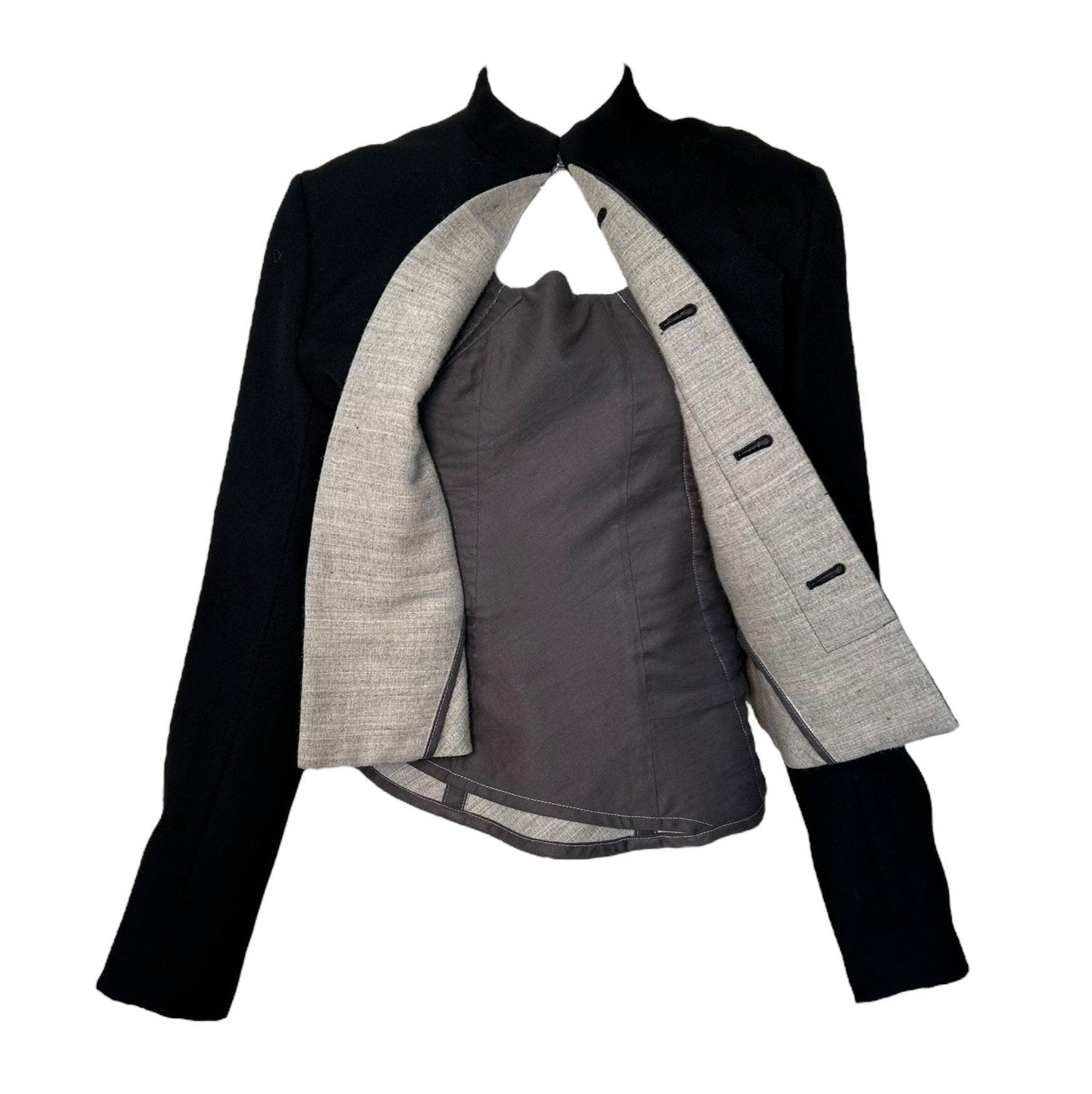 Dieser kühne Wollblazer aus der A/W-Kollektion 1998 von Comme des Garcons strahlt mit seinem einzigartigen asymmetrischen Unterbau architektonische Eleganz aus. Der innen liegende Haken, der ein Korsett mit Klappe vortäuscht, verleiht dem