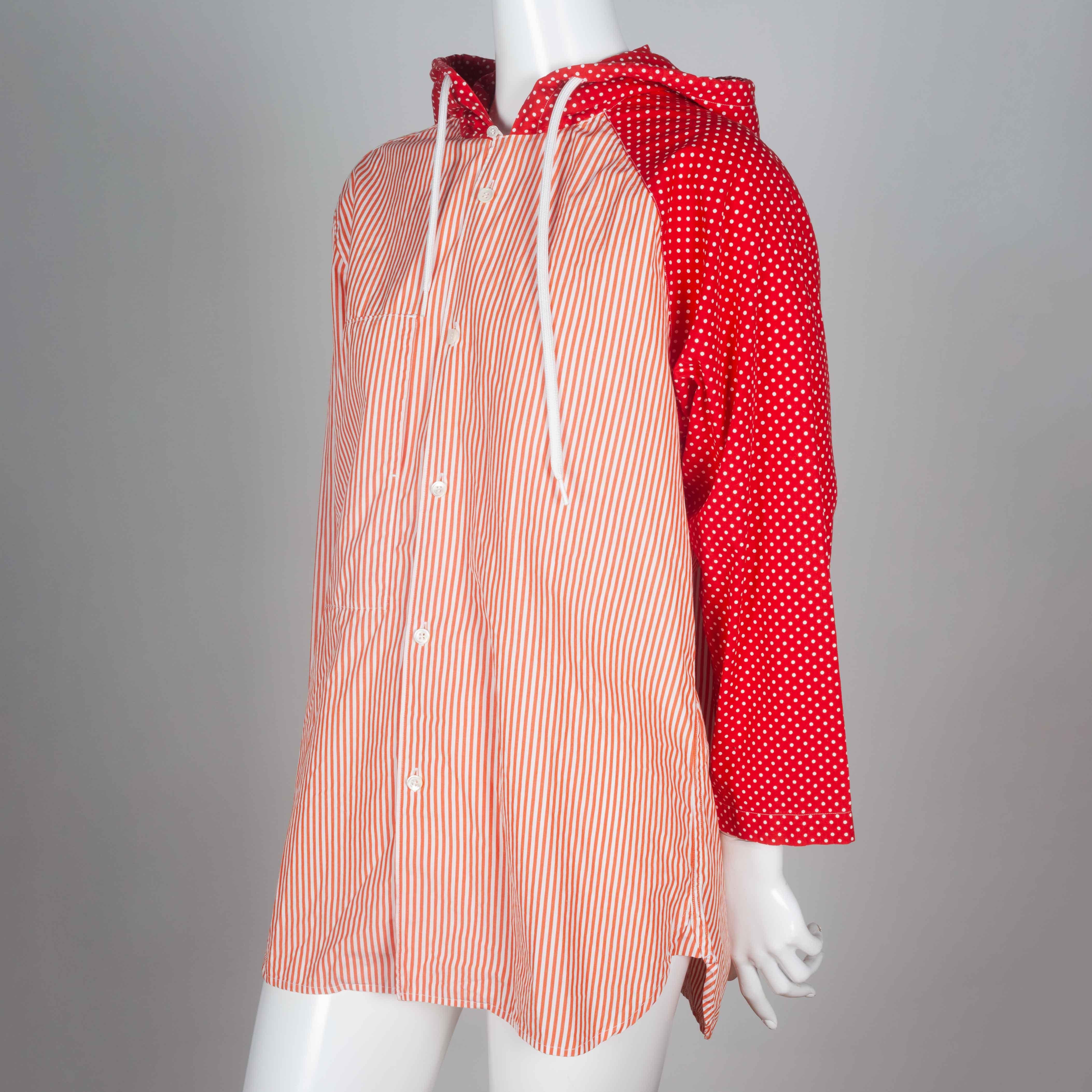 Comme des Garçons red and white poplin shirt with draw string hood and asymmetric pattern. A raglan sleeve with red and white polka dot pattern on one side carries on to the hood, completing the rest of the shirt that is in red and white pinstripes.