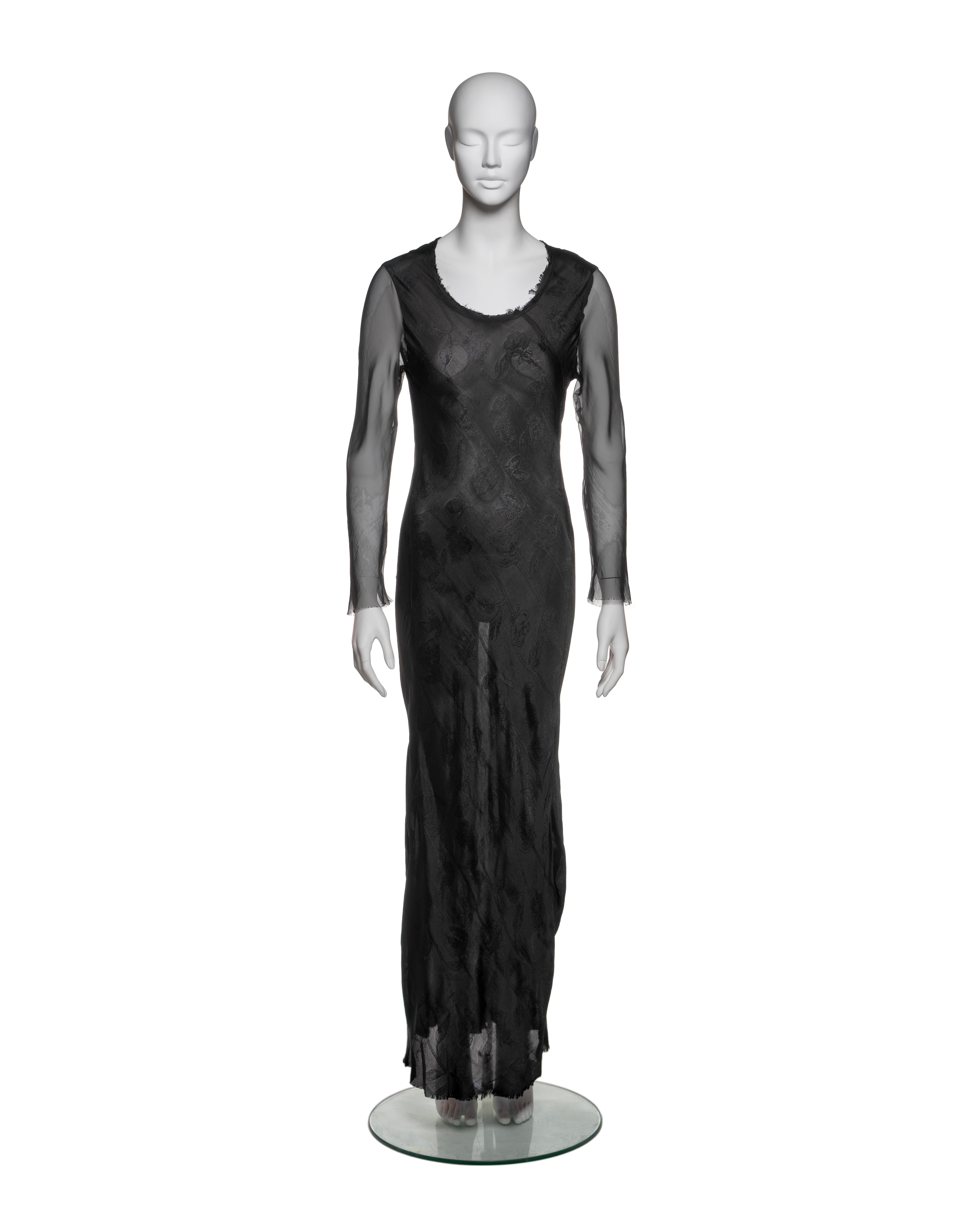 This Comme des Garçons dress from the Fall-Winter 1993 collection features a body made from a black jacquard fabric with a subtle floral pattern, offering a relaxed, floor-length silhouette. The sleeves are crafted from a contrasting sheer silk