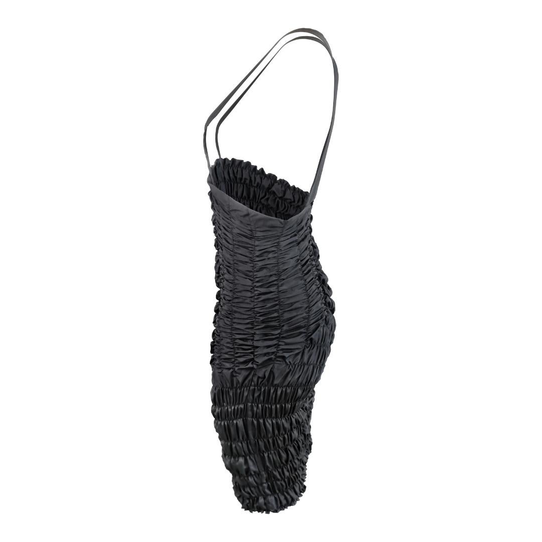 This striking Comme des Garçons smocked bib dress from 1989 showcases Rei Kawakubo's signature avant-garde approach to fashion. The dress features an intricately gathered smocking technique throughout, creating a textural, voluminous silhouette that