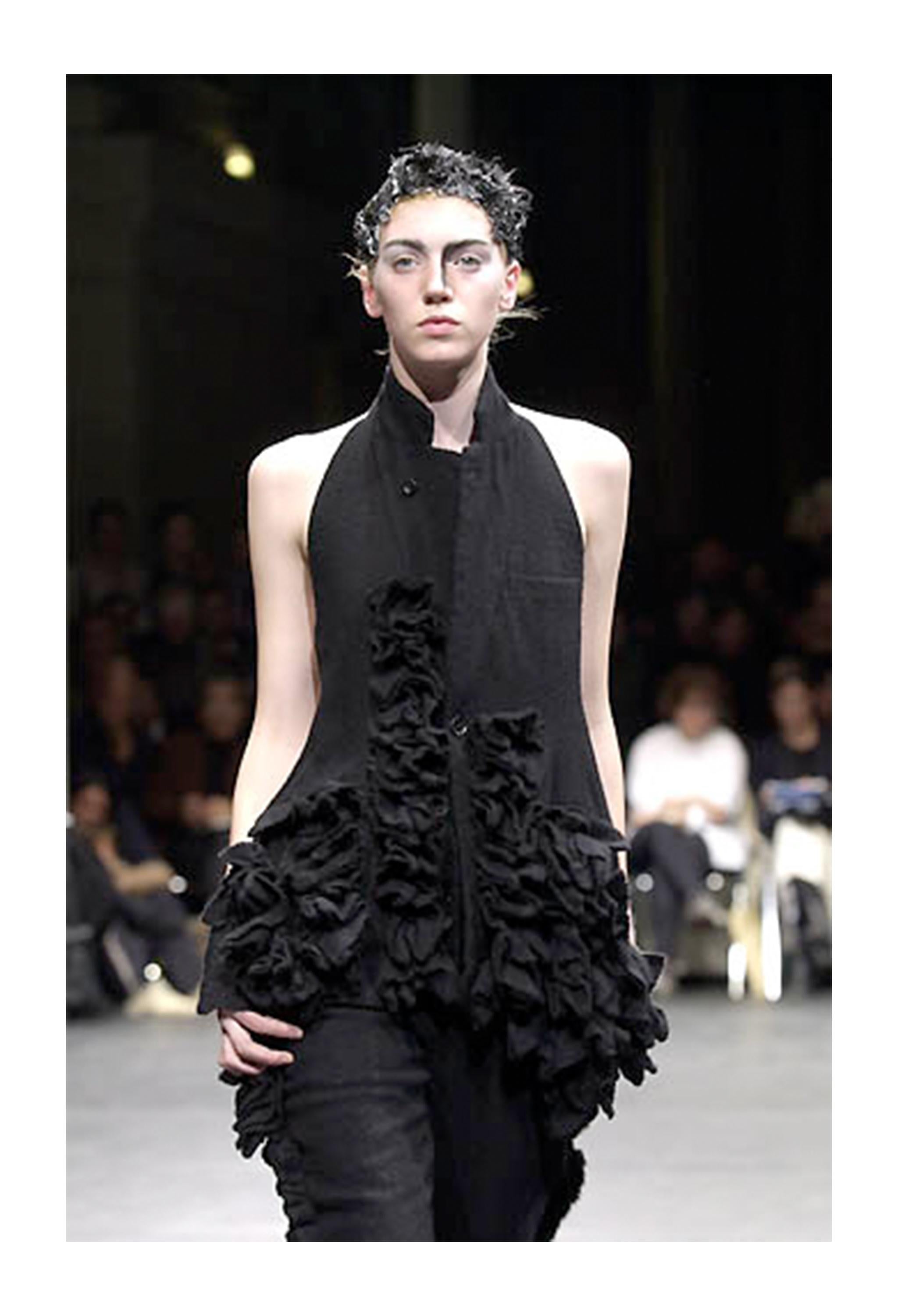 Resurrection Vintage è lieta di offrirti un gilet vintage in lana nera di Comme des Garçons caratterizzato da schiena aperta con cinturino in pelle, dettagli con volant, profondo scollo a V, design monopetto e due tasche frontali con patta.  

Comme