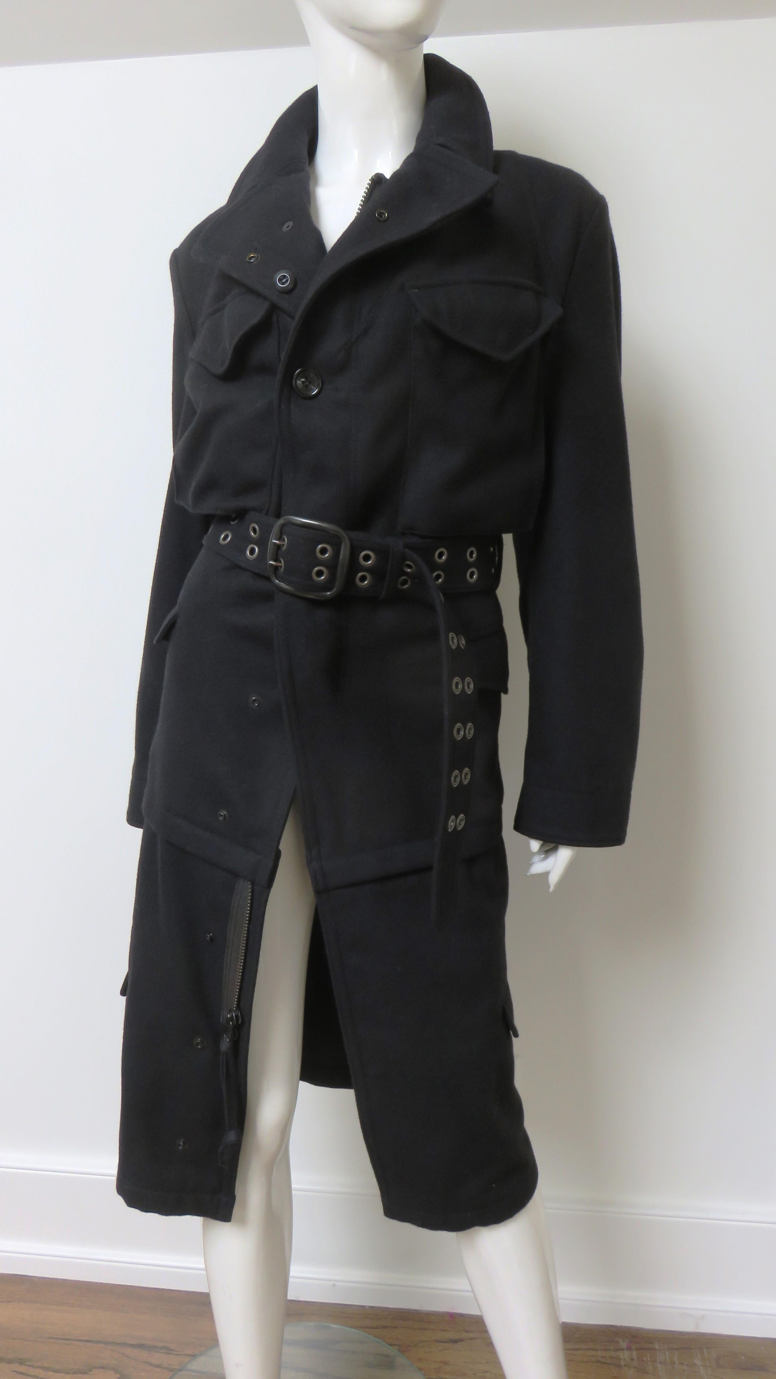 A fabulous black wool coat by Junya Watanabe for Comme des Garcons the AD 2006 collection. It is abundant in elaborate detail including a matching grommet belt, chest patch pockets, hip and knee level flap pockets, and adjustable cuffs.  It has a