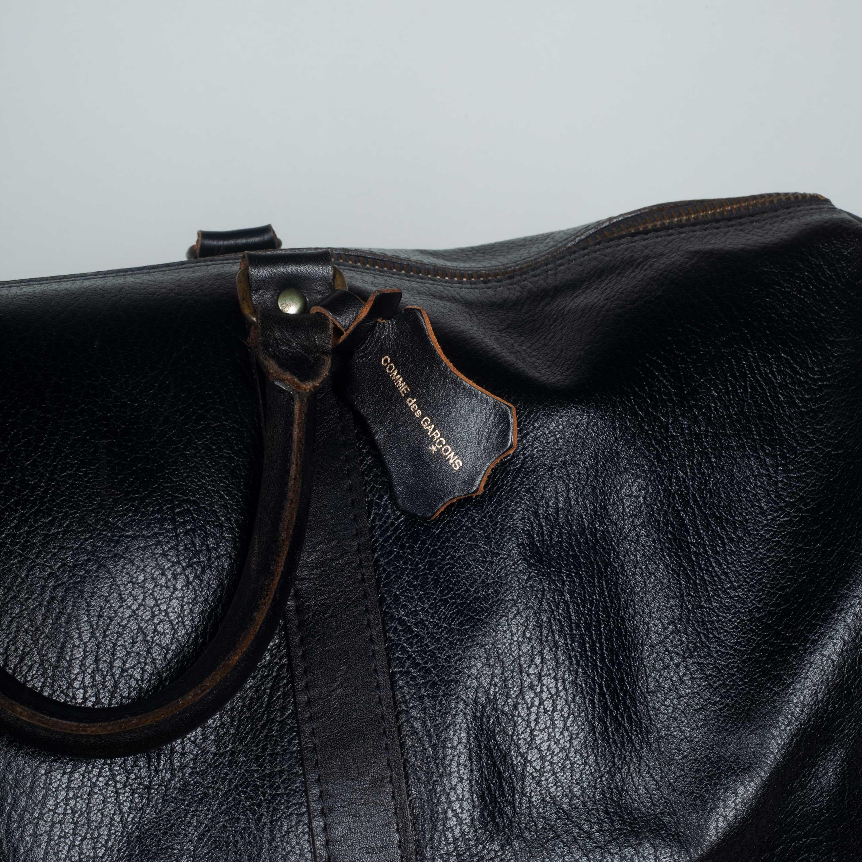 Comme des Garçons large, black leather Boston bag from Japan with zip closure, natural cowhide interior and leather tag with logo. This stylish vintage travel bag can be used as a carry-on for short trips or long. It is large enough to hold garments
