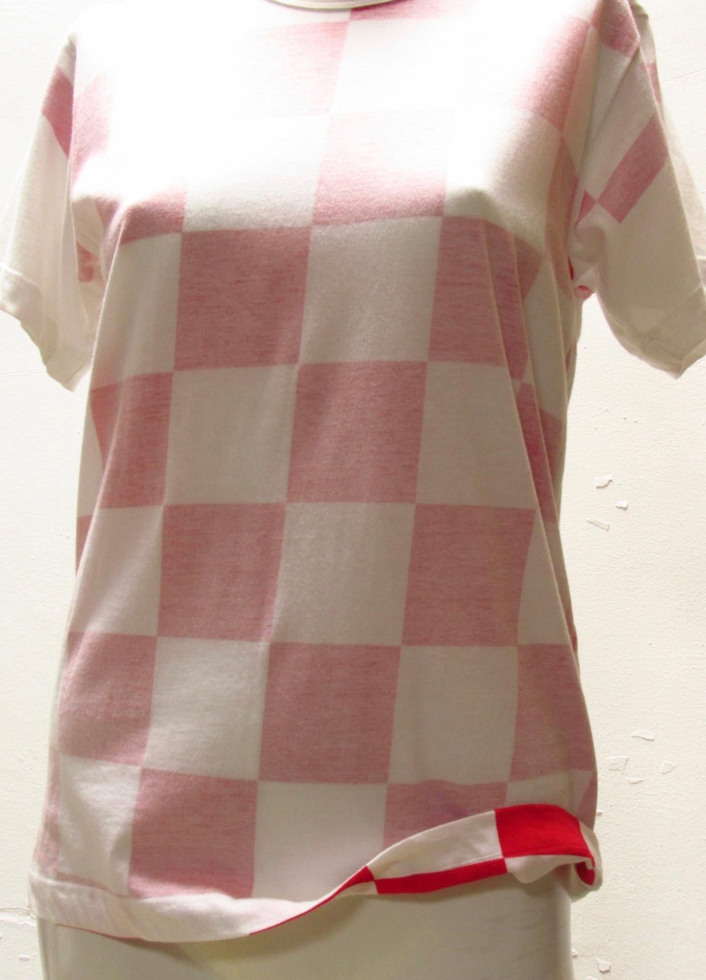 A basic white cotton tee from vintage Comme Des Garçons becomes more playful when constructed with the inside out, only hinting at the red checkerboard pattern printed on the reverse side of the fabric. Back is white. Shirt hangs to hip length. 