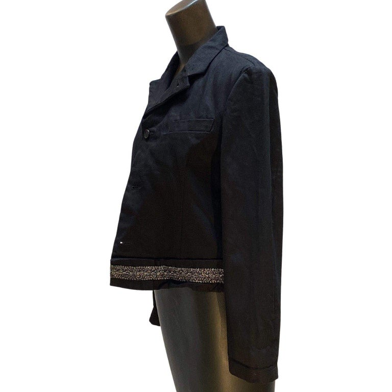 This structured and cropped black Comme des Garçons jacket is contstructed of heavy cotton and features a single breast pocket and dazzling metallic trim detailing along the hemline.
