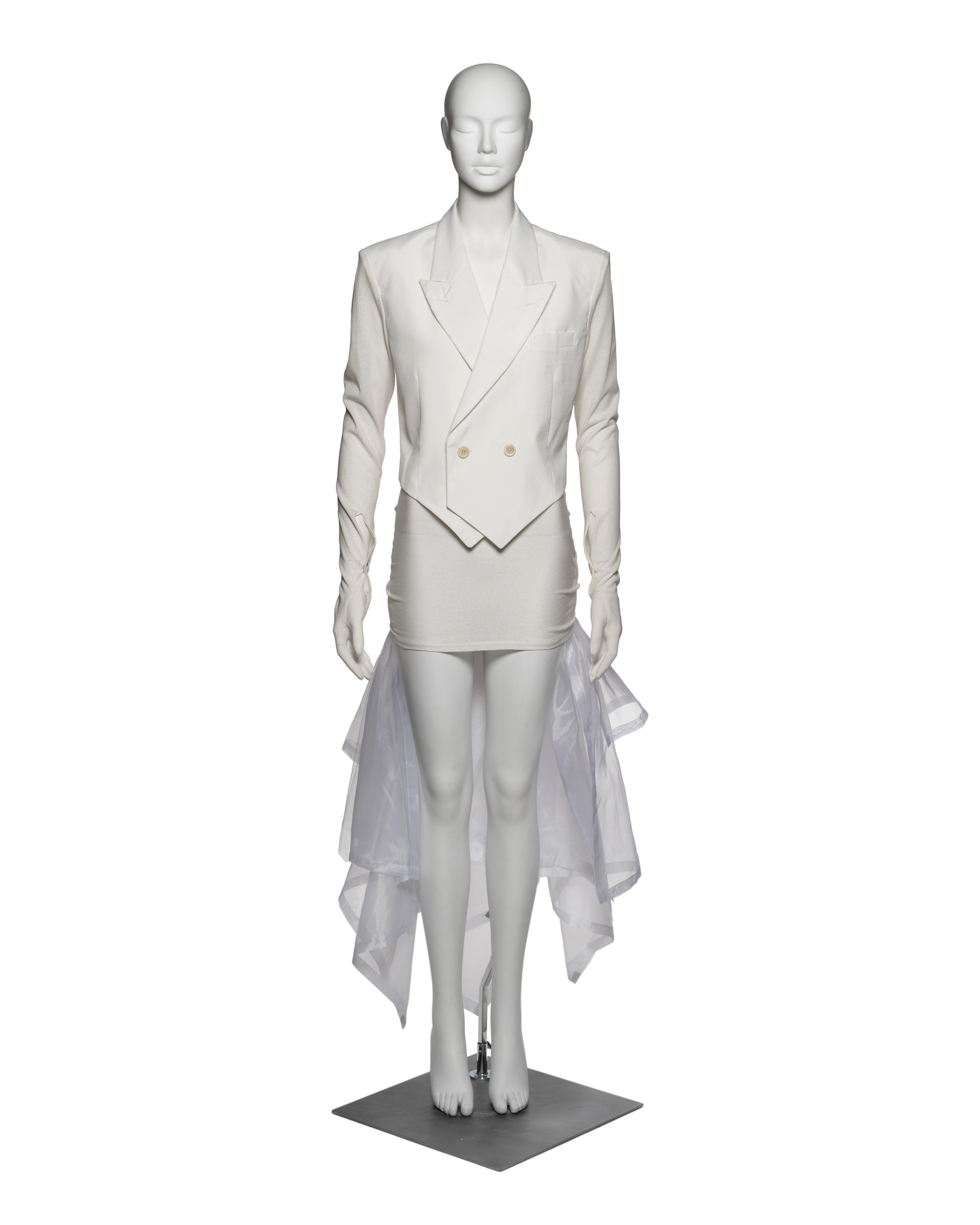 Bridal ensemble by Rei Kawakubo for Comme des Garçons, from the Fall-Winter 1987 collection. Comprising a sharply tailored, double-breasted cropped jacket in ivory cotton twill, paired with a stretch jersey mini skirt with a layered white organza