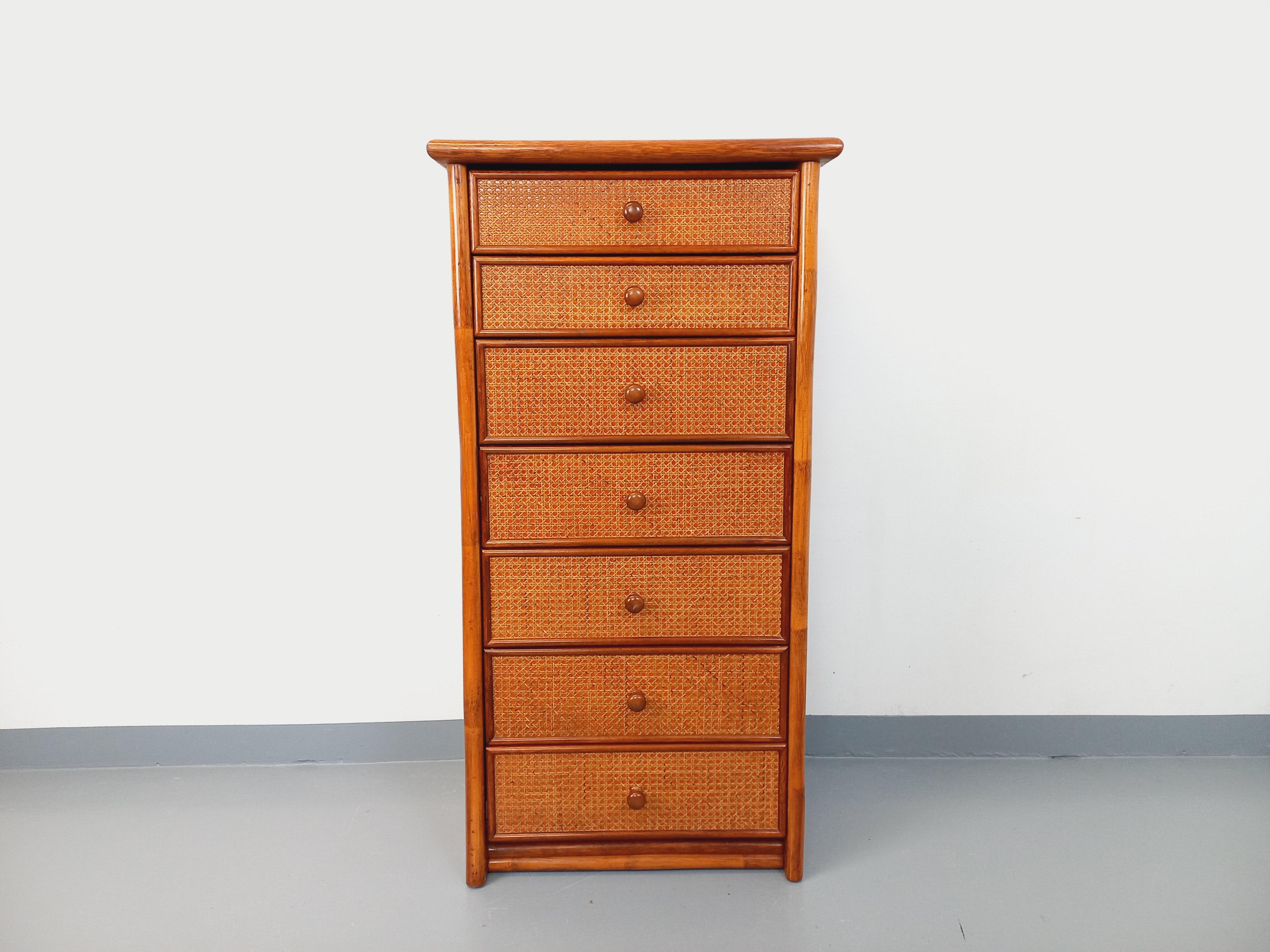 Commode chiffonnier semainier vintage des années 70, en rotin, bois et cannage, 7 tiroirs à coulisses, 2 petits et 5 grands, intérieur des tiroirs en mélaminé, fond du cannage couleur vermillon, très bon état général avec quelques signes du temps