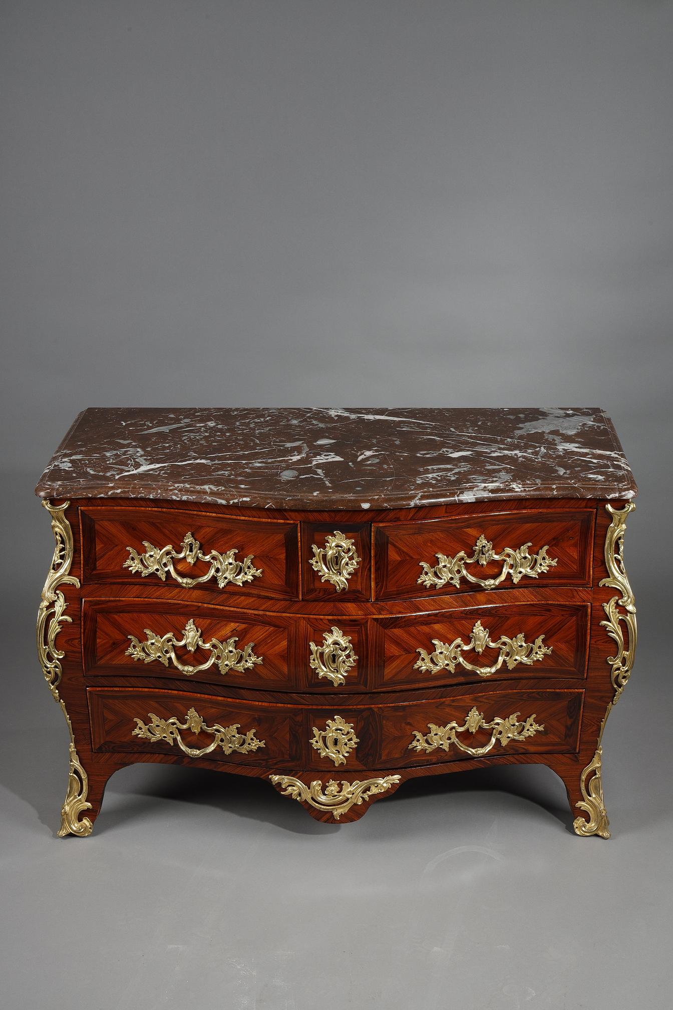 Commode grave en placage de bois de violette ouvrant à quatre tiroirs sur trois rangs. Richement décoré de bronzes rocaille ciselés, tels que chutes, sabots, poignées de tirage, entrées de clé et tablier. Il est surmonté d'un plateau en marbre rouge