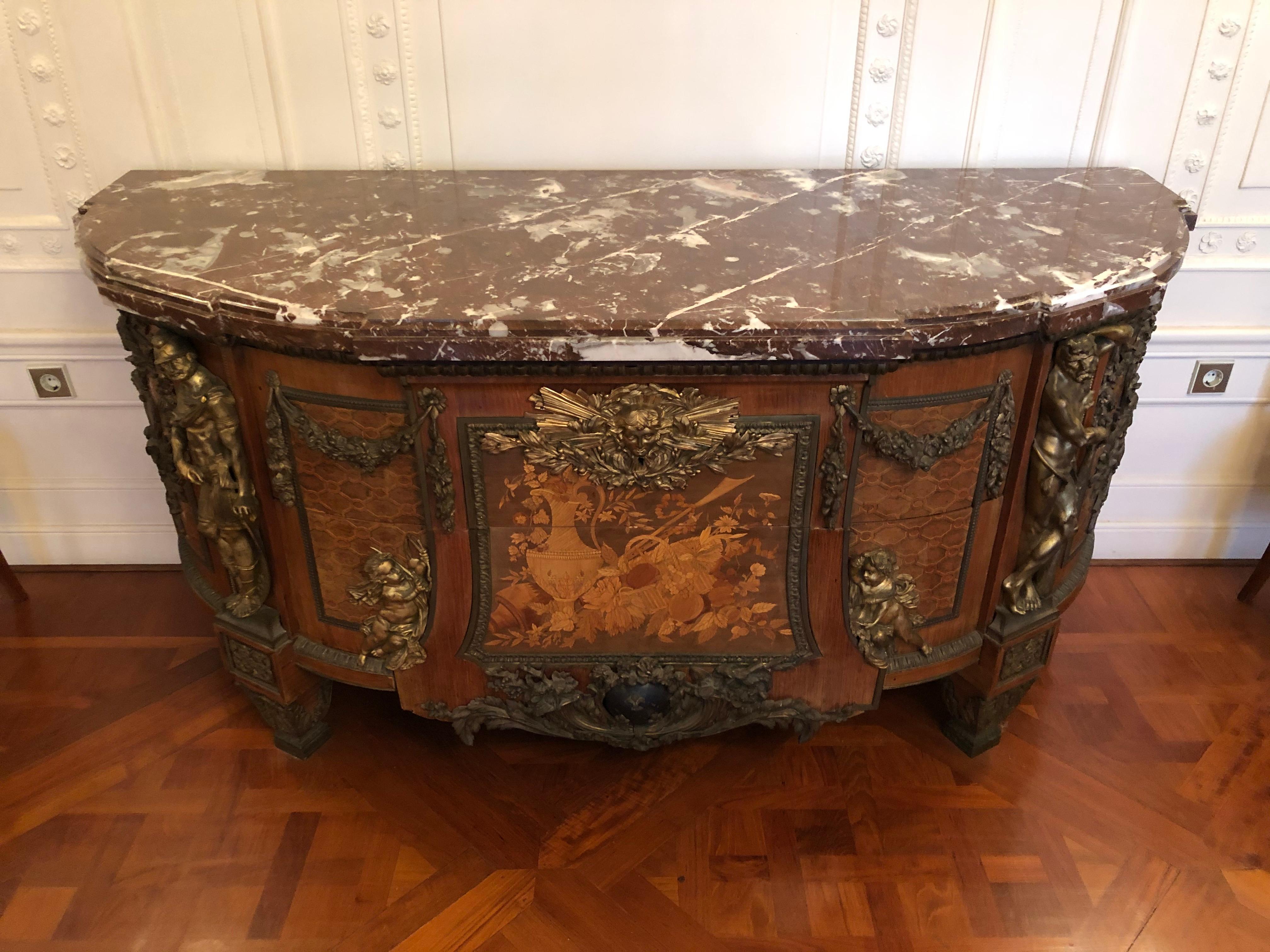 Made in hardwood, of a splayed half-ellipsoid form, with marquetry latticework in mahogany and further fine woods, with two “sans traverse” drawers with floral marquetry on a trapezoid panel, large lavish bronze mounts on the angles and sides
