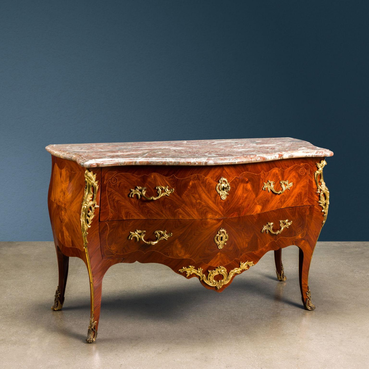 Commode a due Cassetti continui con catena a scomparsa. Il mobile è bombato grazie ad una mossa sia verticale che orizzontale, completamente impiallacciato in Bois de Rose quadripartito steso trasversalmente in modo da formare i tipici cuori; una
