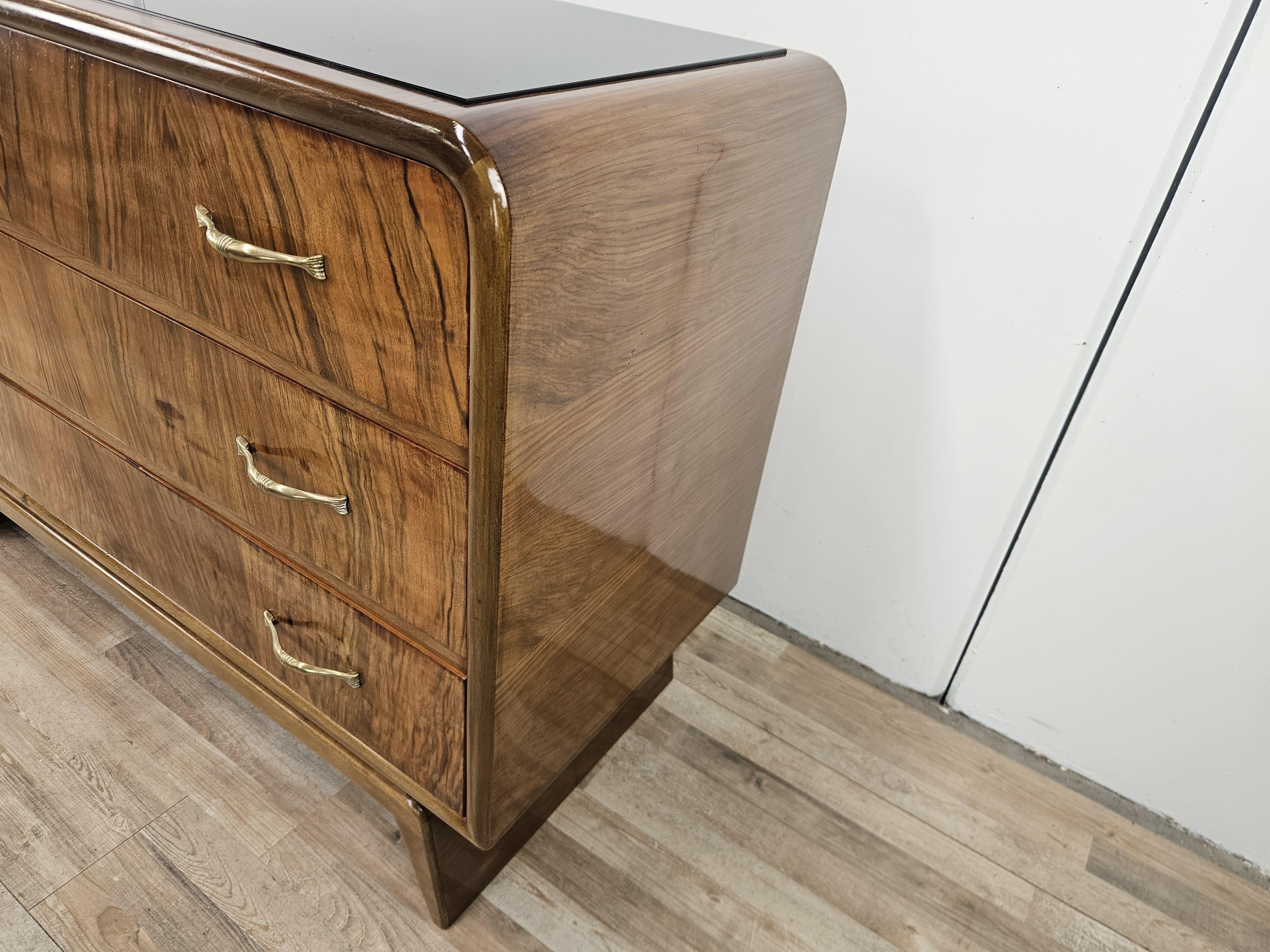 1940s Art Deco dresser with three large, sturdy drawers, covered in walnut burl with black glass top on top.

The dresser features an elegant design, structure supported by a simple and linear base.
Brass handles original to the period.

Presents