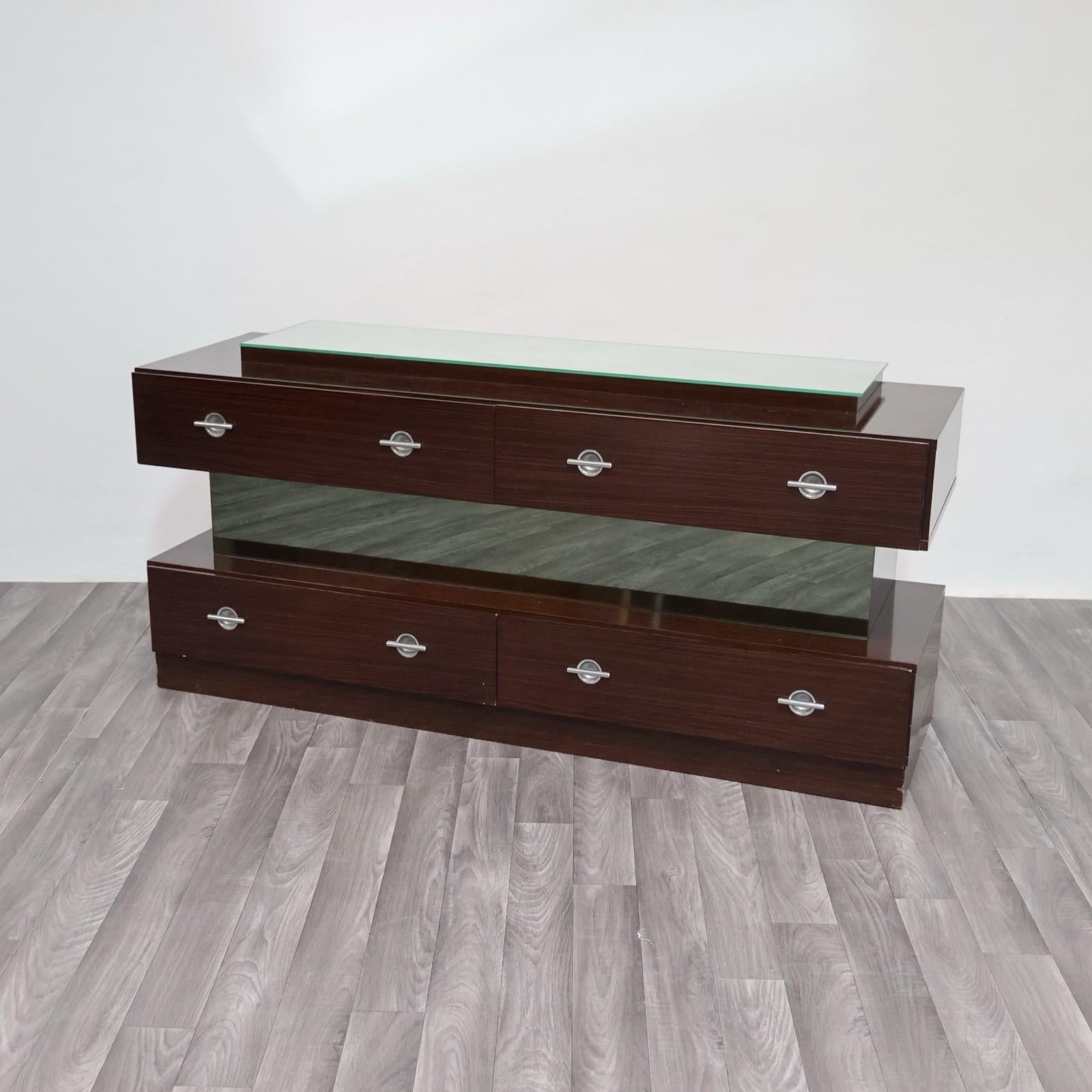 Elegante Comò in Ebano Macassar, realizzato negli anni ’80, caratterizzato da un raffinato design cubico dalle linee essenziali e contemporanee. La struttura geometrica è scandita da quattro cassetti sovrapposti, separati da una lastra frontale in