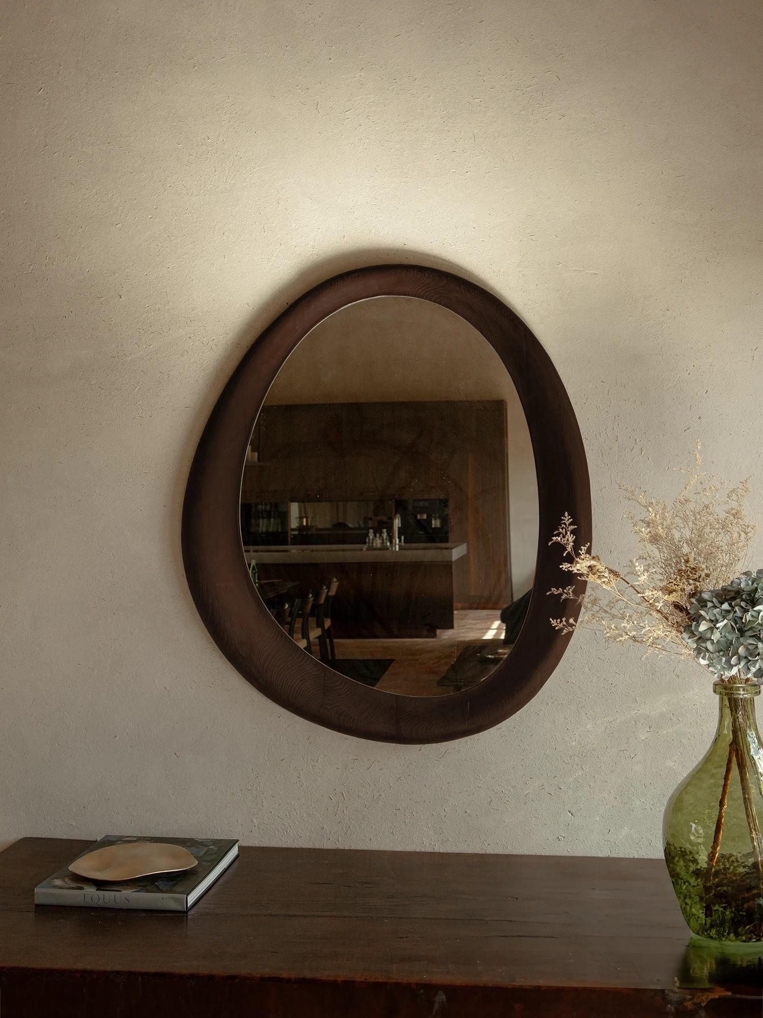 Part of the Smooth Collection, this wall mirror embodies the harmony of sculptural form and functional design. Its soft, organic silhouette is framed in a minimalist wooden profile, offering a refined presence that feels both modern and timeless.