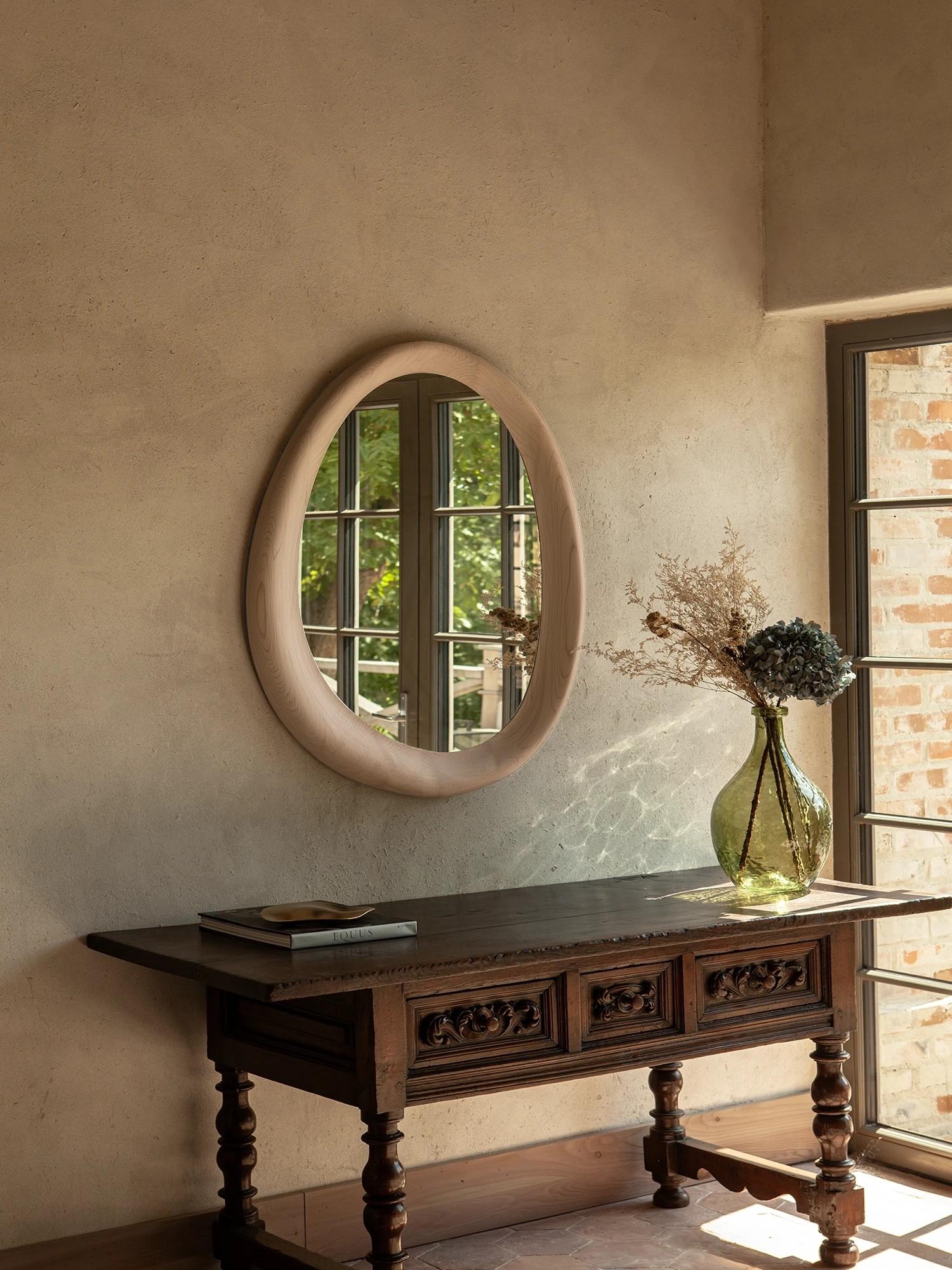 Part of the Smooth Collection, this wall mirror embodies the harmony of sculptural form and functional design. Its soft, organic silhouette is framed in a minimalist wooden profile, offering a refined presence that feels both modern and timeless.