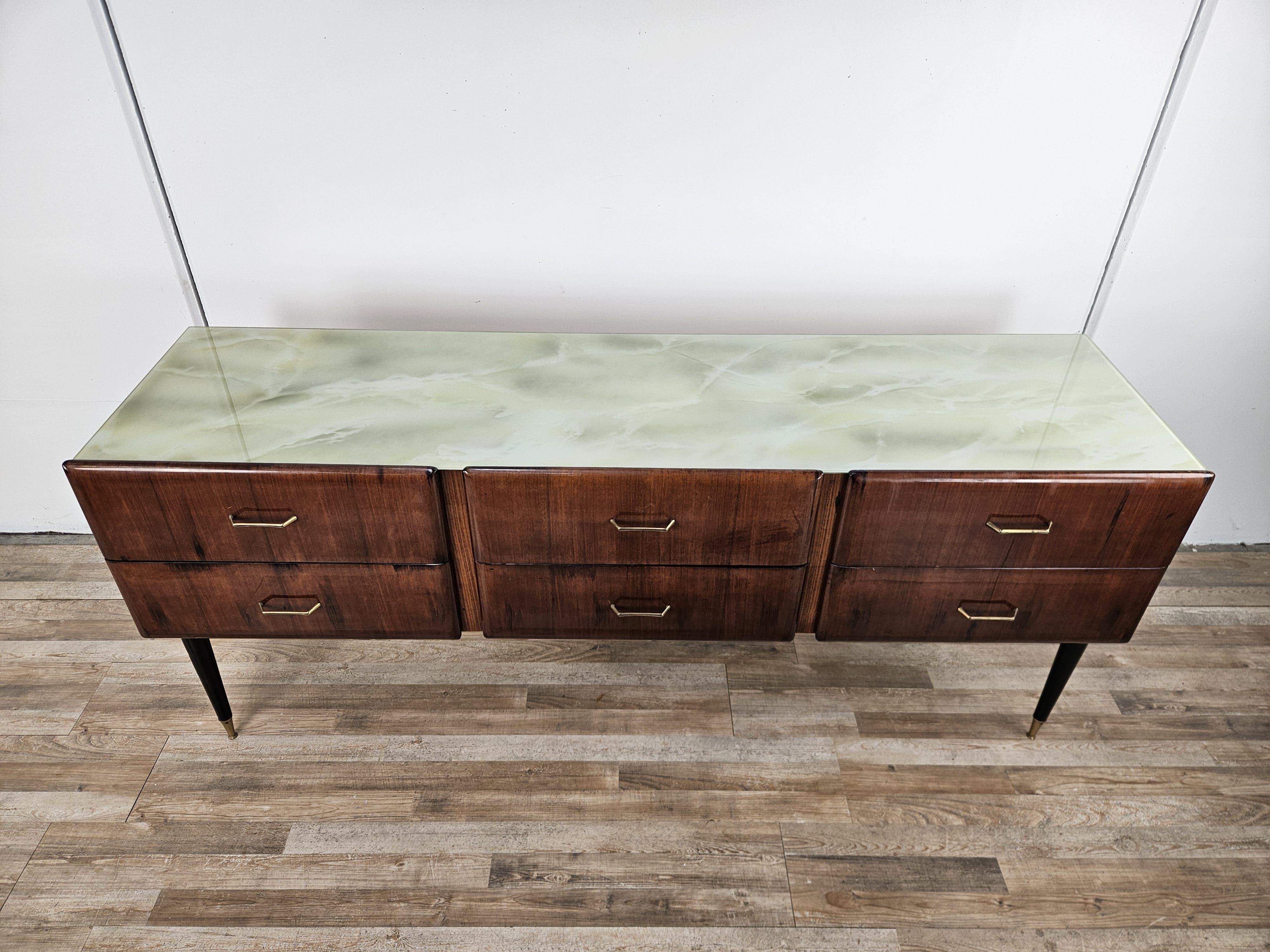 Vintage 1960s dresser covered in mahogany burl with six large, sturdy drawers.
The cabinet has an ornate and worked glass top, the drawers have original brass handles of the period, and an additional special feature are the height-adjustable