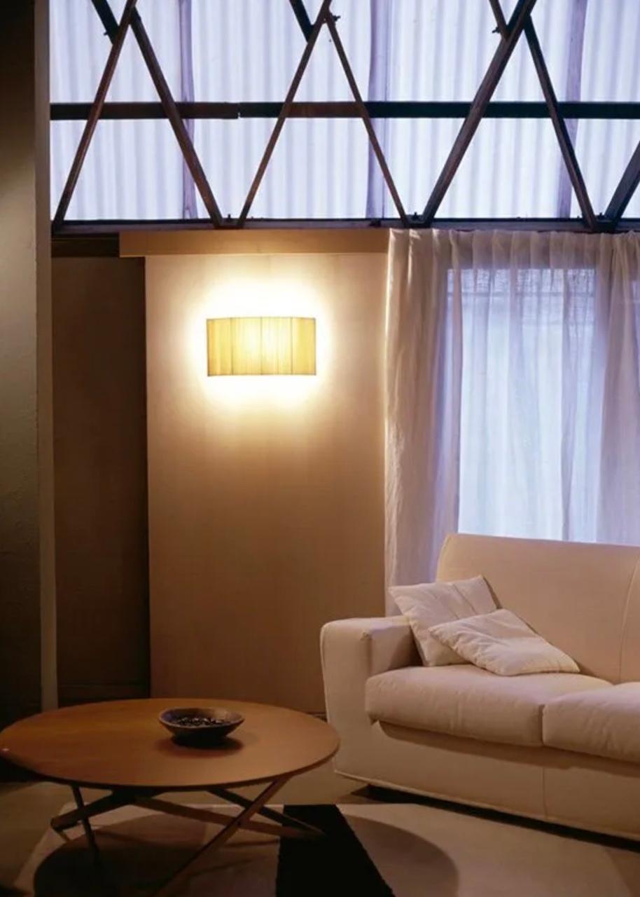 This minimalist wall lamp humanizes neutral spaces with its colorful and functional sobriety. The shade is fondly hand-ribboned, piece by piece. Switched on, it provides a characteristic warm light, rich in nuances, and switched off, it is a small,