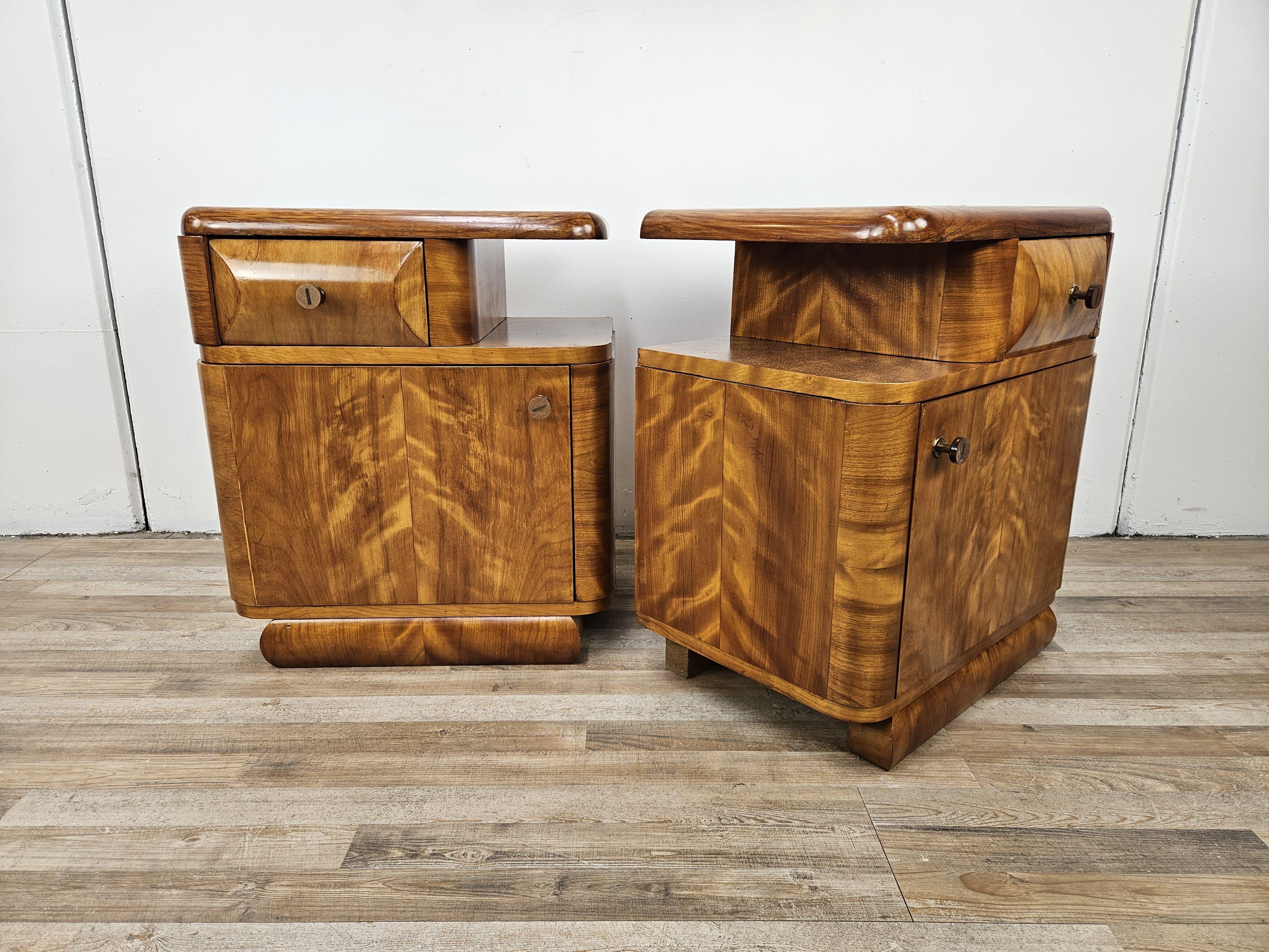 Paire de tables de chevet Art Déco des années 1940 en ronce de noyer blond avec tiroir et grand compartiment de rangement avec étagère intérieure.

Poignées en bois originales de l'époque, très distinctives et élégantes.

Les tables de chevet ont