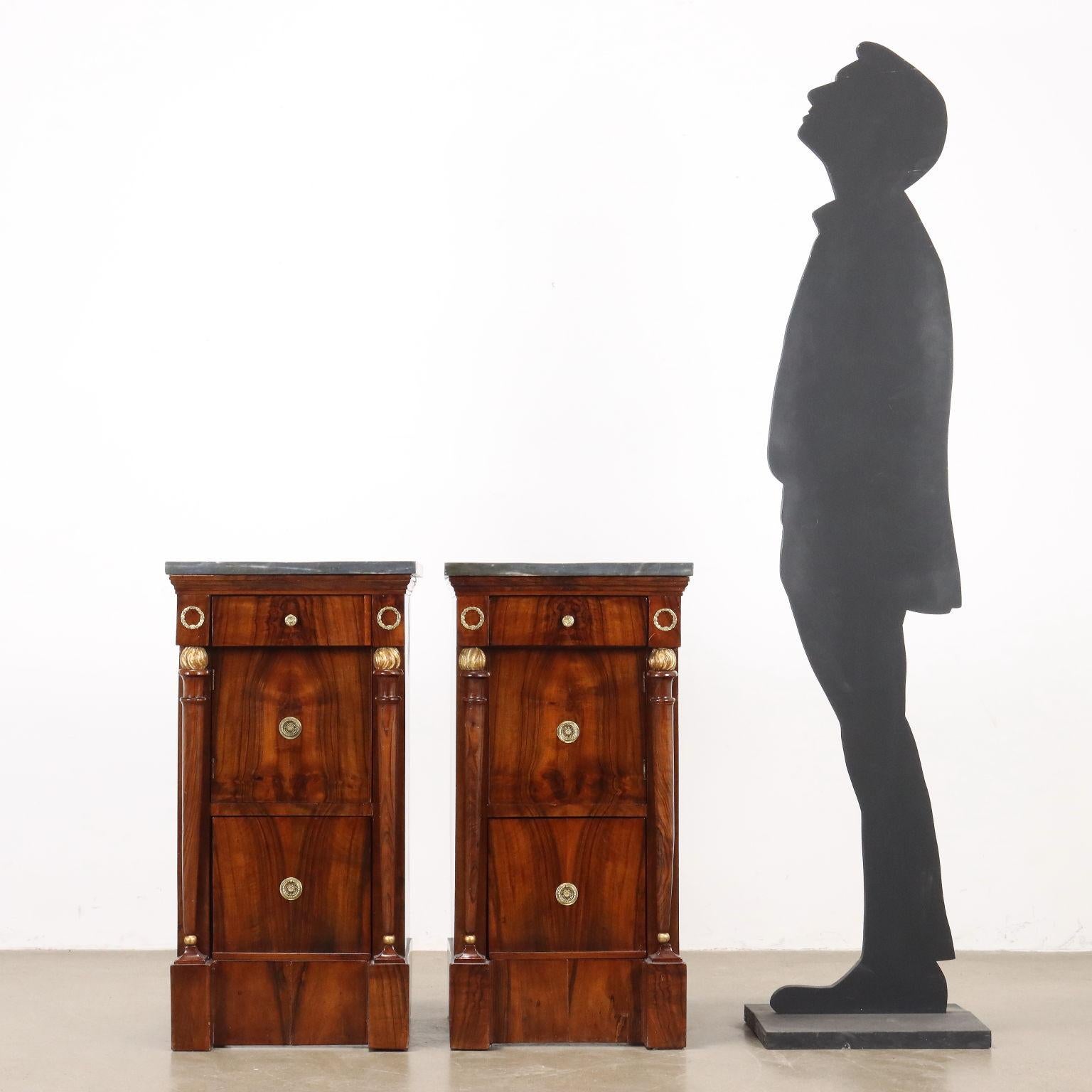 Coppia di comodini del periodo Impero, in noce lastronati in noce rigatino fiammato, presentano sul fronte un cassettino sotto piano, un anta e al di sotto un cassetto più profondo. Piedi a plinto reggono sui montanti, colonne composta da fiaccola