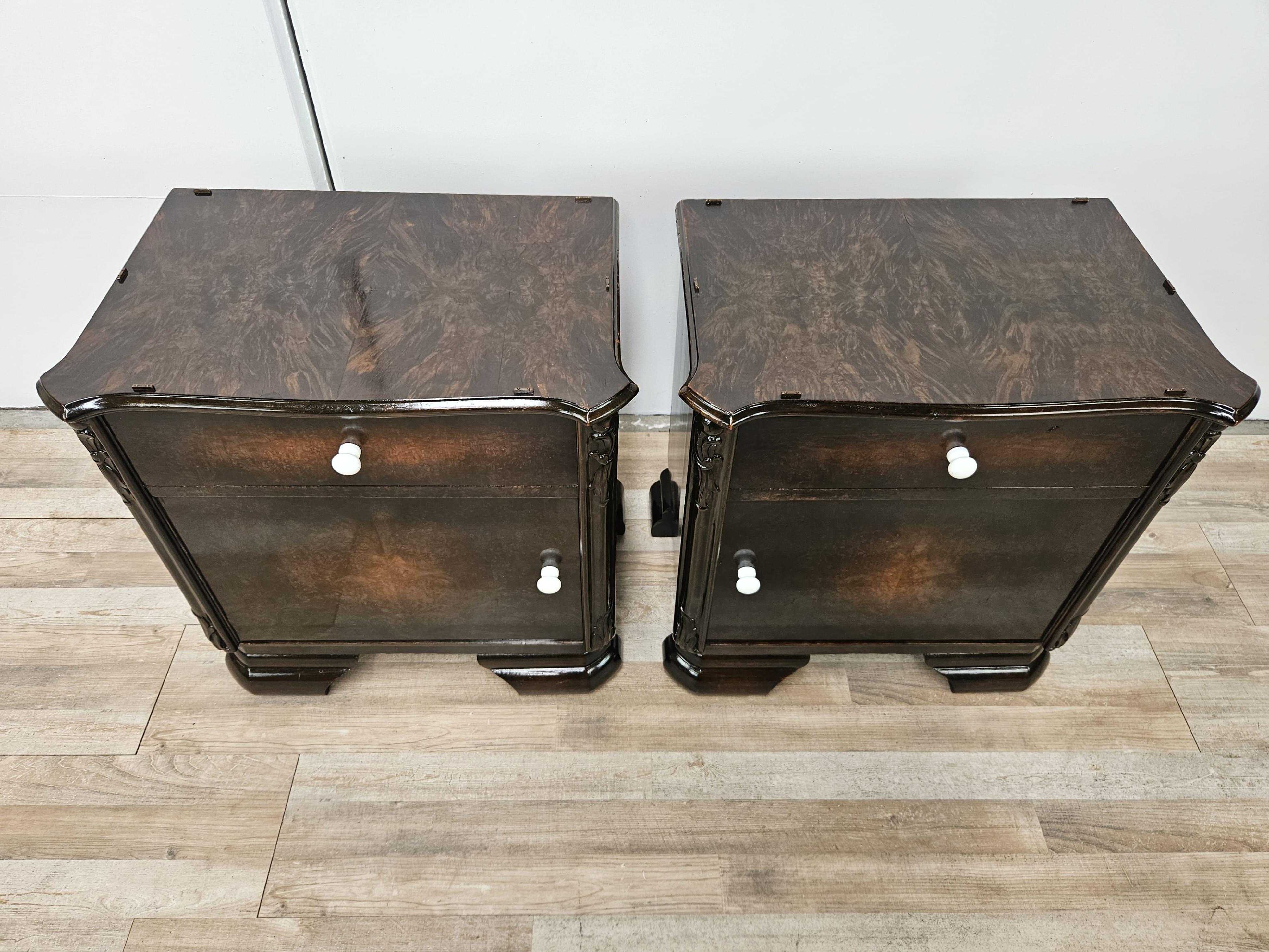 Pair of wooden bedside tables dated circa 1940, very compact in their measurements and finely decorated with carvings along the doors and drawer.

White lacquered wood knobs to give contrast and a tonal break.

Against the light they have some marks