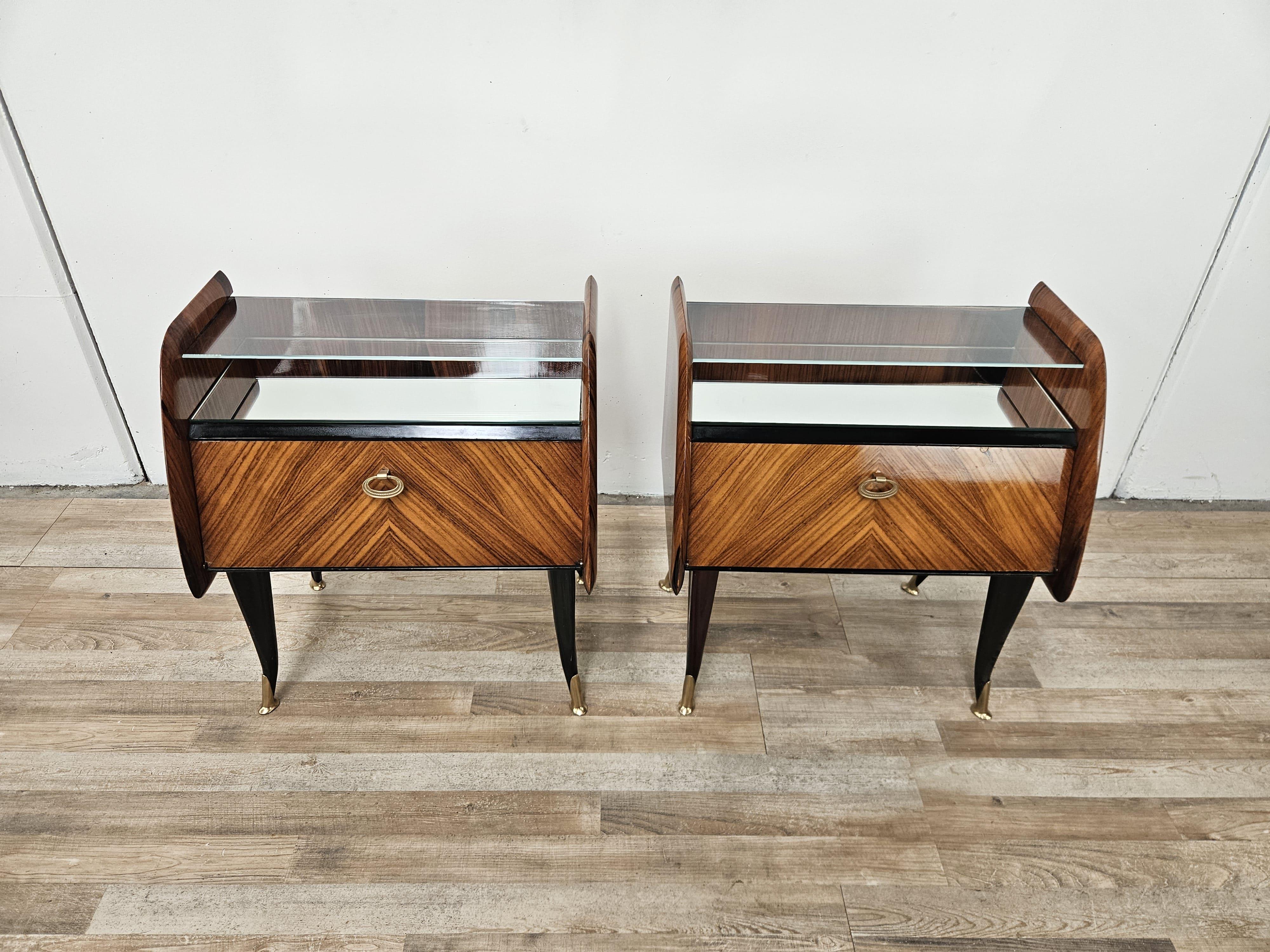 Mesillas de noche vintage de los años 50 revestidas de caoba con puerta abatible y compartimento interior.

Elegante y bien acabado, nótese la parte superior espejada bajo el pequeño cristal transparente y los raíles de latón de los pies.

Las